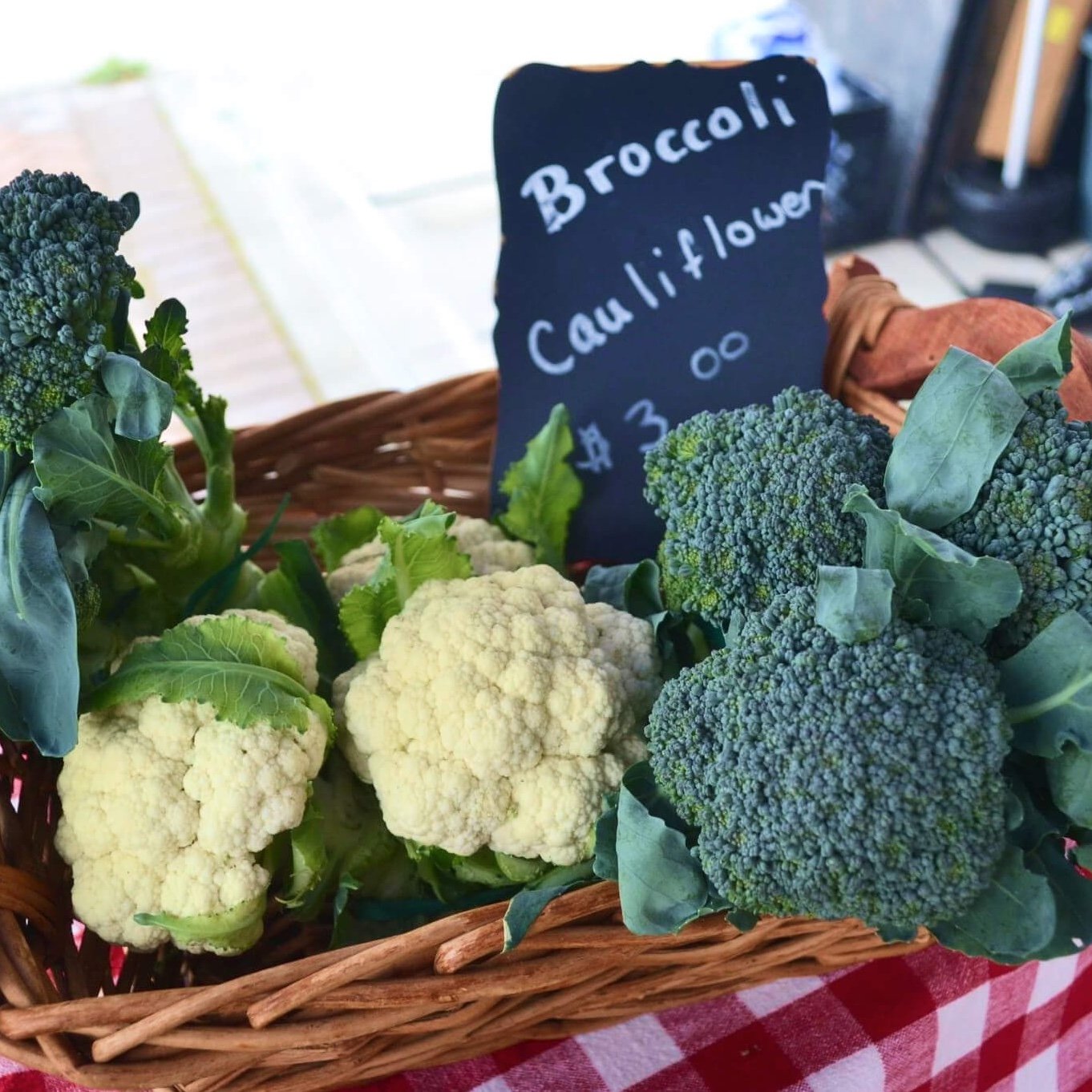 Basket with broccoli and cauliflower, price sign $3.00, on a red-patterned cloth.