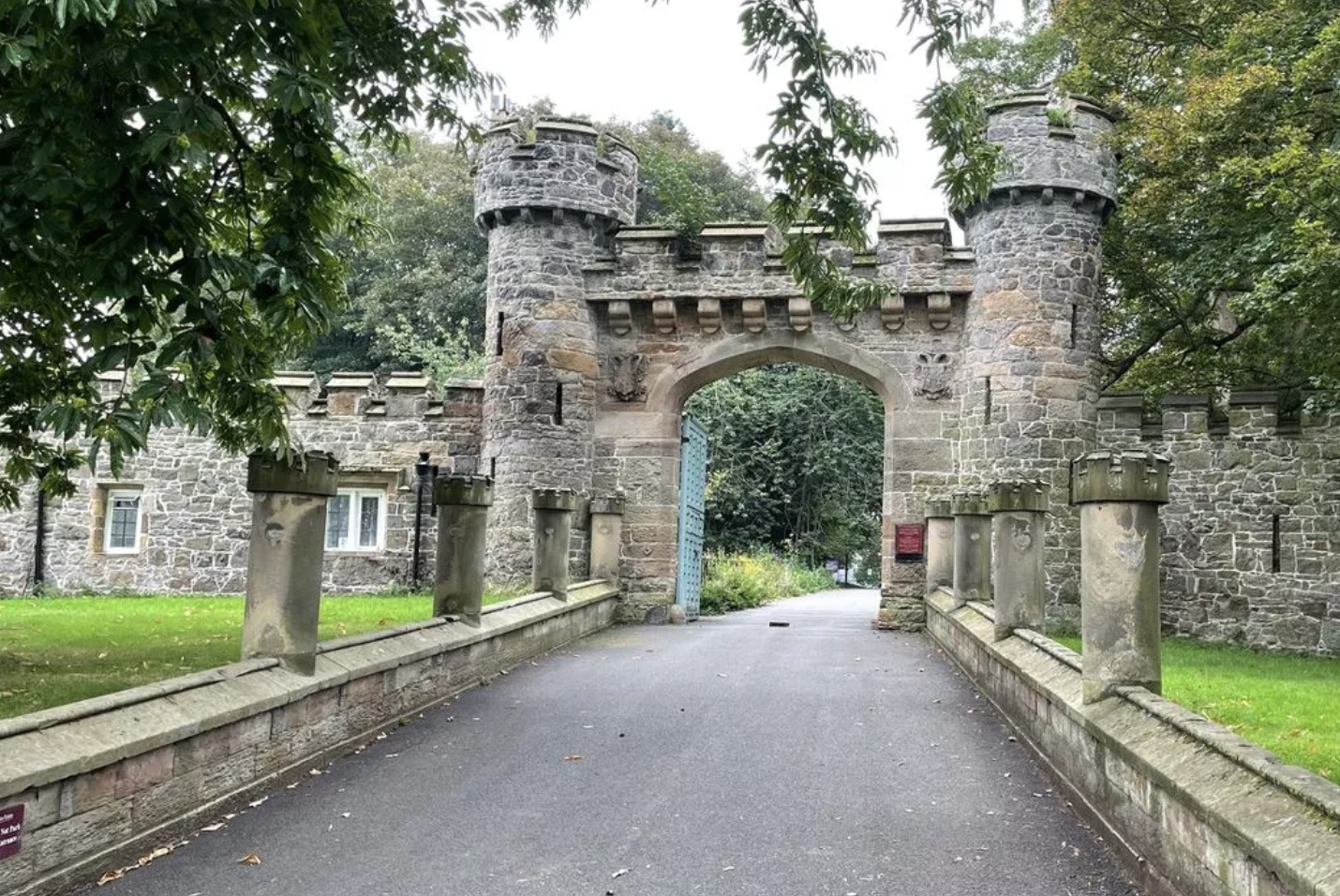 Stone castle gate with a blue door, surrounded by green trees and grass in Hawarden.