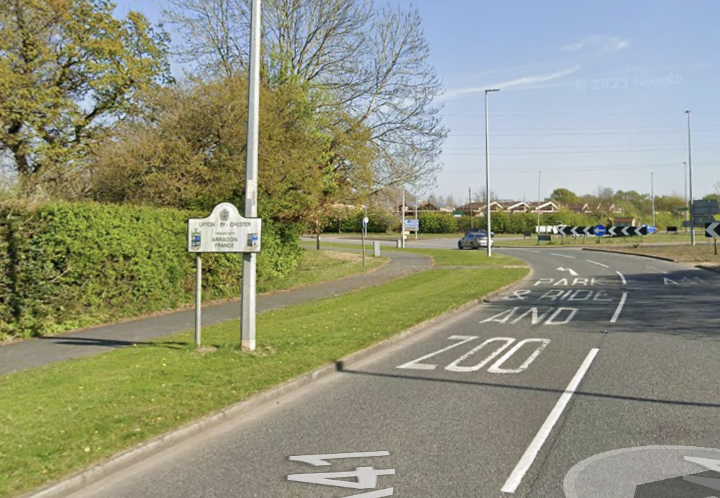 A roundabout with a car approaching, a sign indicating welcome to Upton, chester