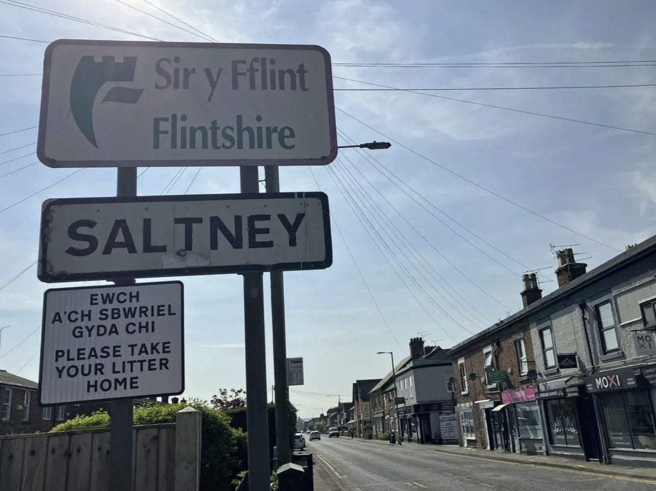 Street signs on a busy town street, indicating Sir y Flint, Flintshire, and Saltney. Additional sign asking residents to take their litter home.