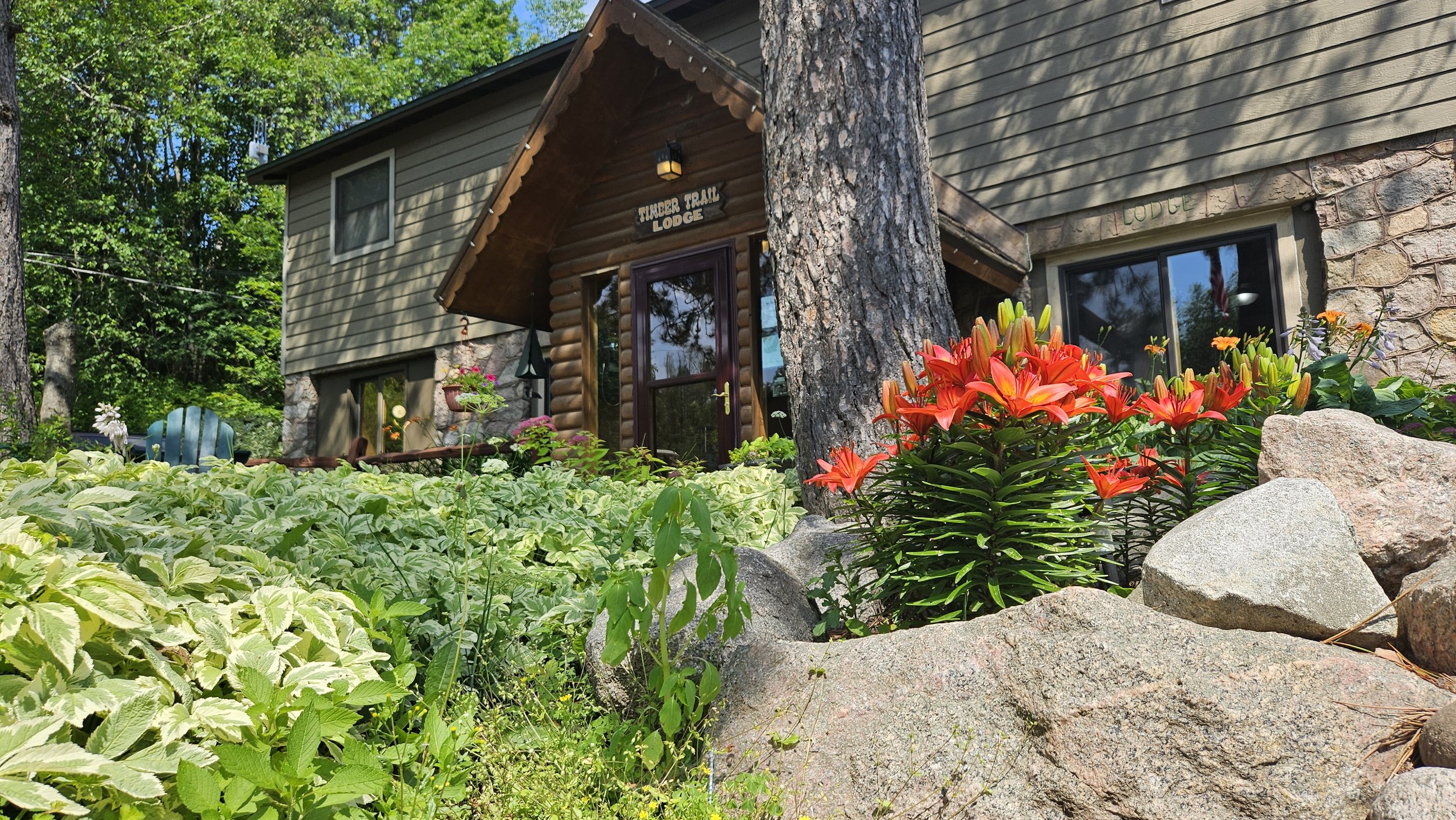 Lodge entrance with stone and wood exterior surrounded by lush plants and red flowers