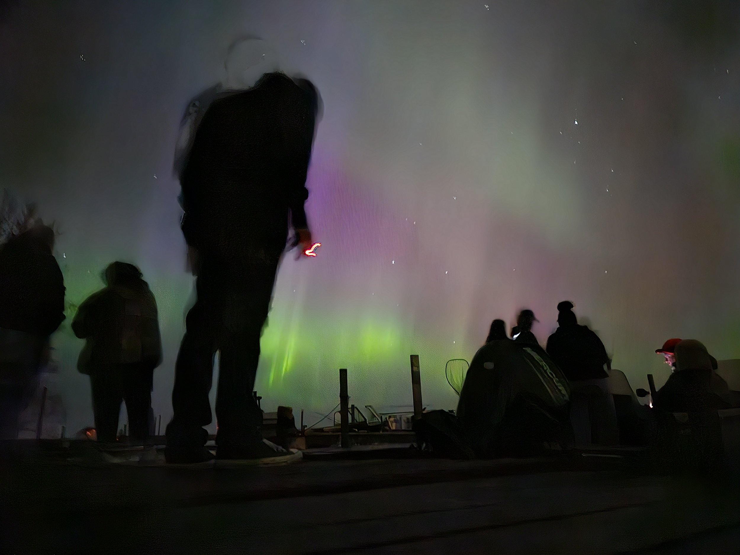 People silhouetted against colorful aurora borealis in night sky