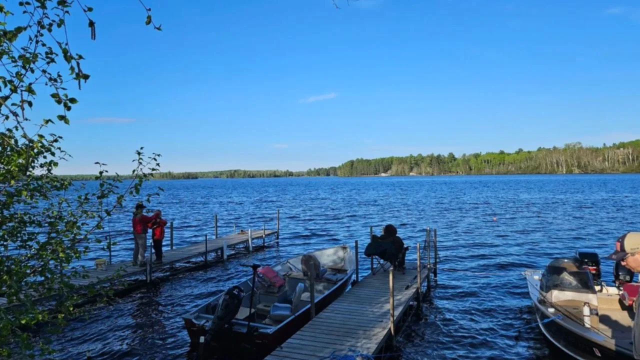Wooden docks at Timber Trail Lodge on Farm Lake with fishing boats, calm blue water, forest shoreline.