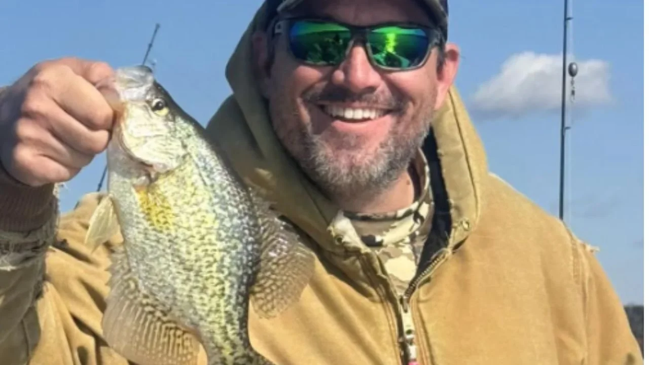 A man smiling and showing the fish he caught.