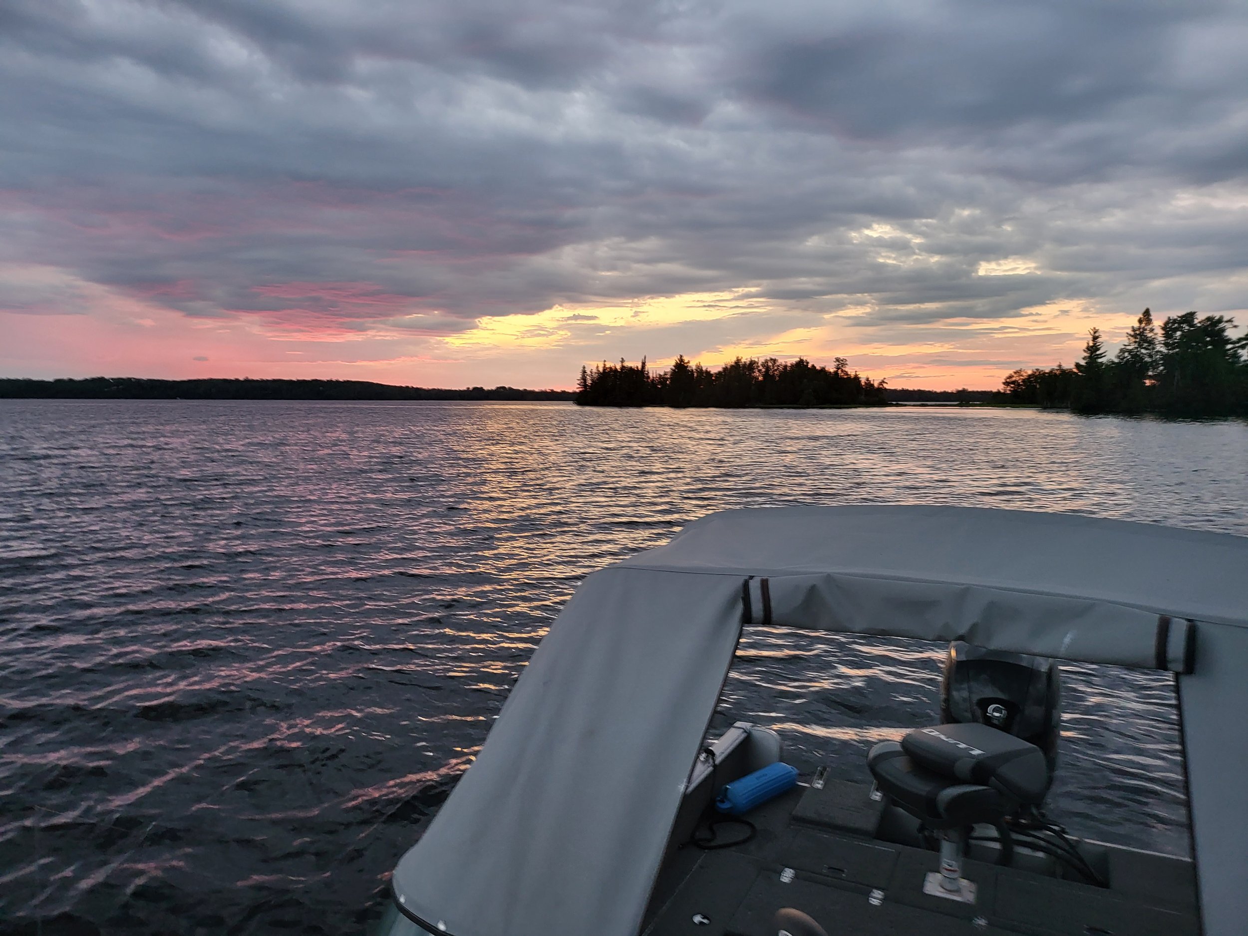 Boat on a lake during sunset with colorful clouds and distant trees.