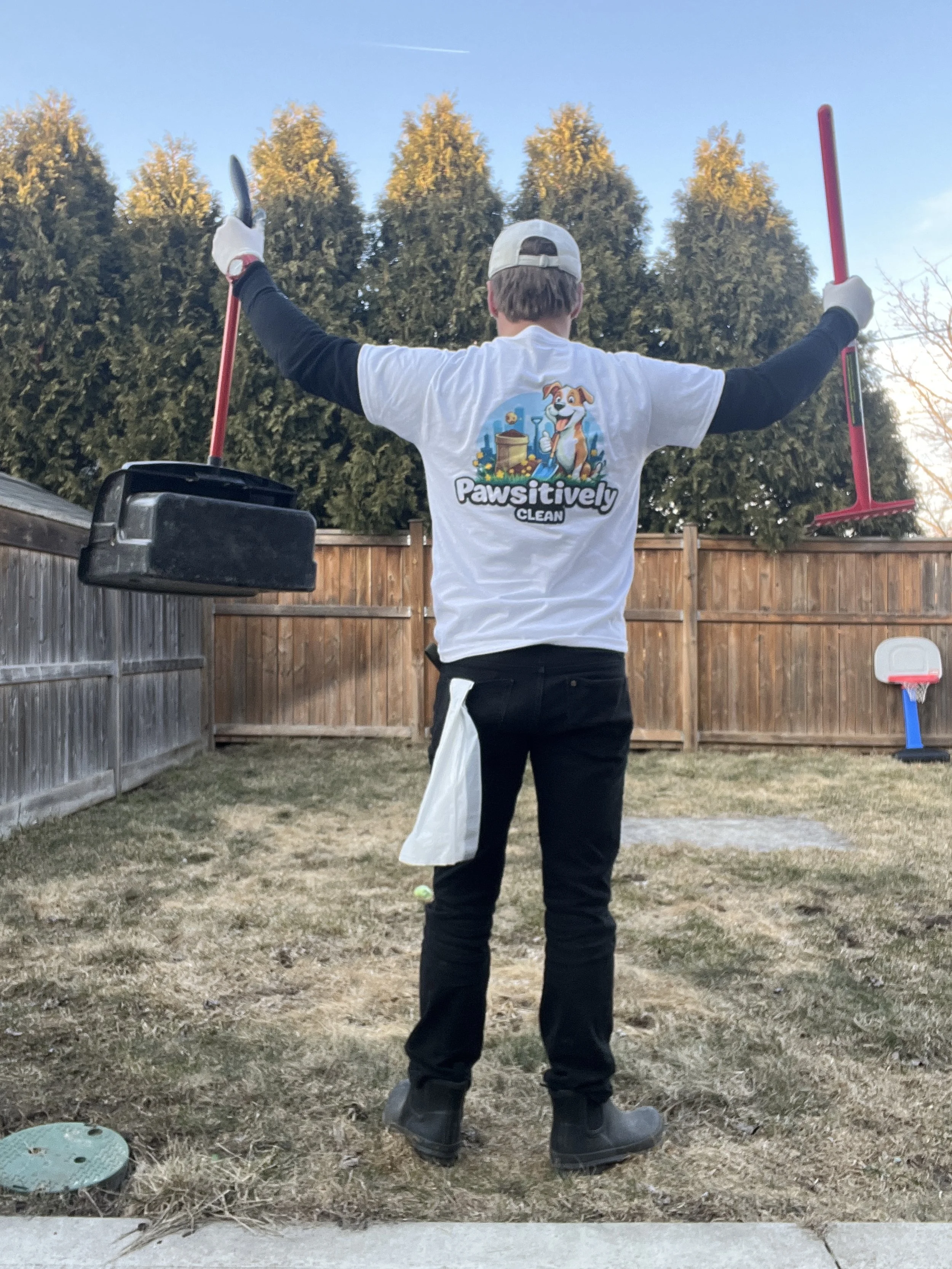 Person wearing a 'Pawsitively Clean' t-shirt holding cleaning tools in a backyard