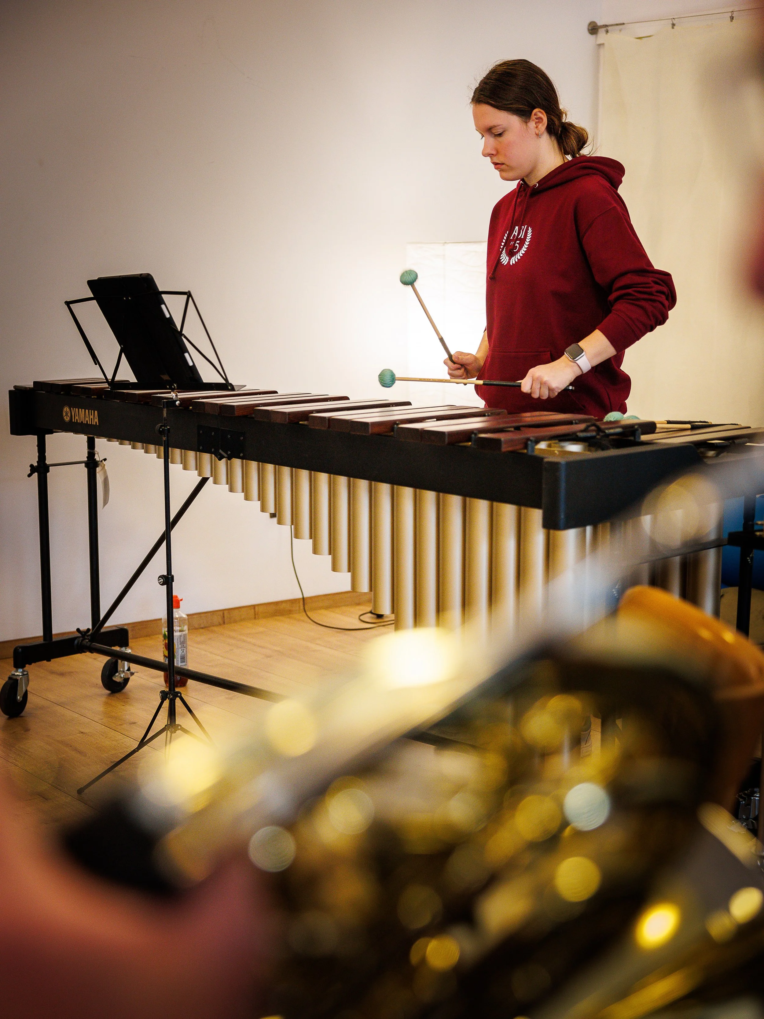 Eine junge Frau spielt auf einer großen elektronischen Xylophon-ähnlichen Trommel, während im Vordergrund ein Teil eines Gold-Instruments unscharf zu sehen ist.