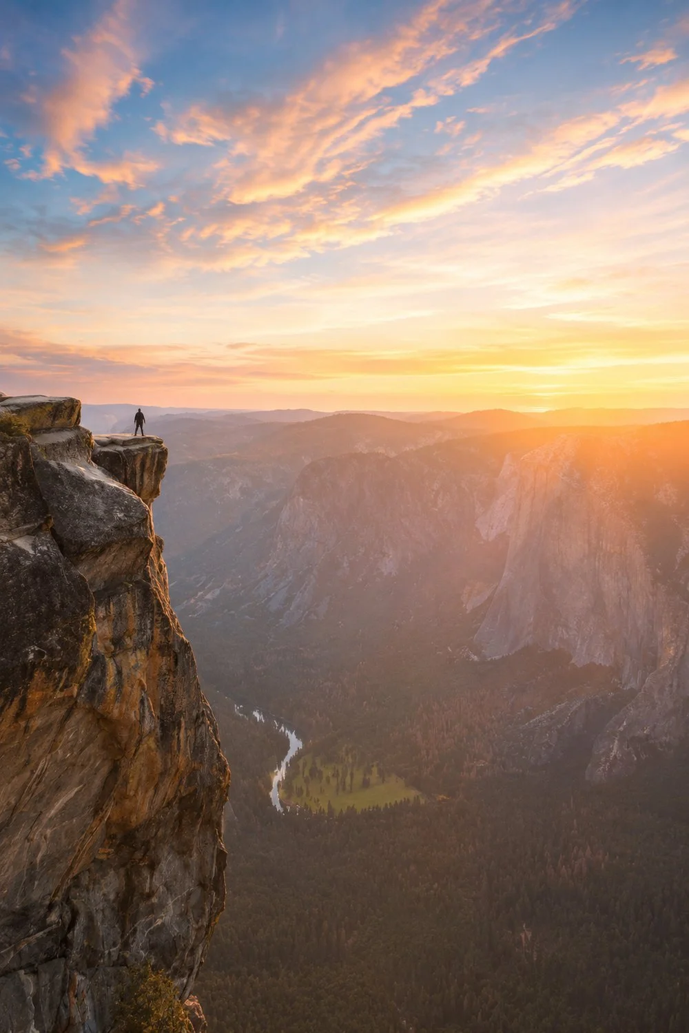 Person standing on a mountain cliff at sunrise, representing perspective, courage, and values-guided trauma therapy in California and Virginia.