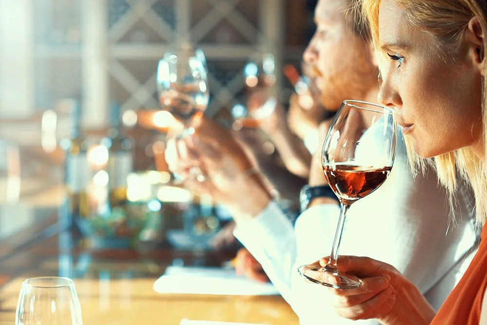 People tasting red wine in a row at a wine tasting event.