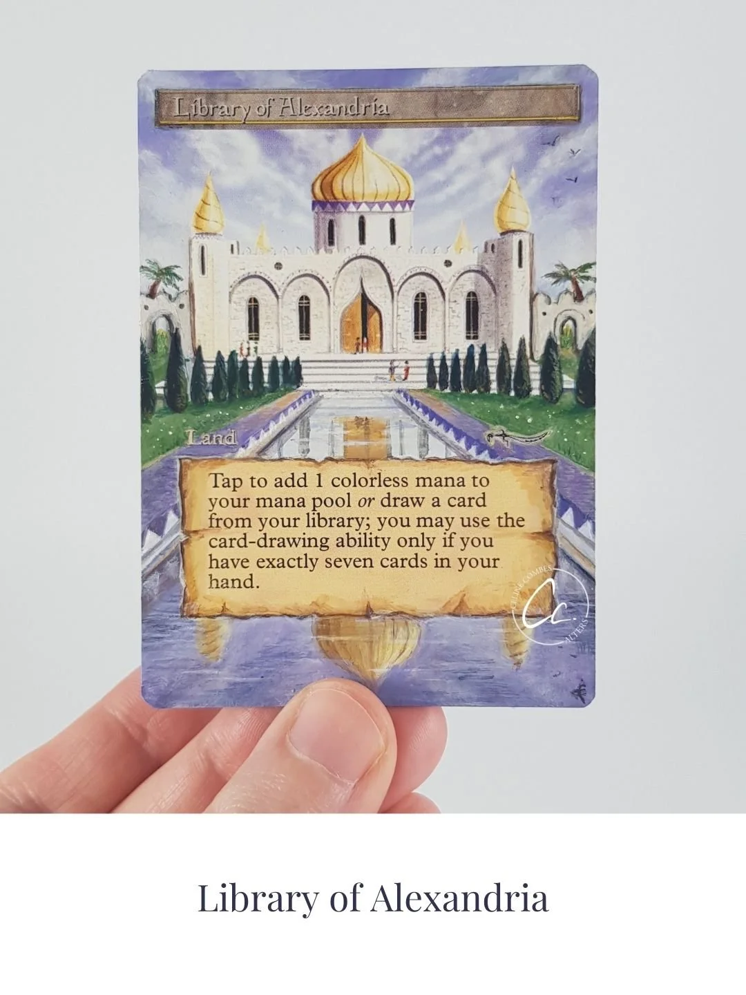 A fantasy-style card titled 'Library of Alexandria' features a palace with a golden dome and minarets, surrounded by greenery and a reflective pool. The card contains game instructions about adding colorless mana or drawing a card from the library, with a signature at the bottom right.