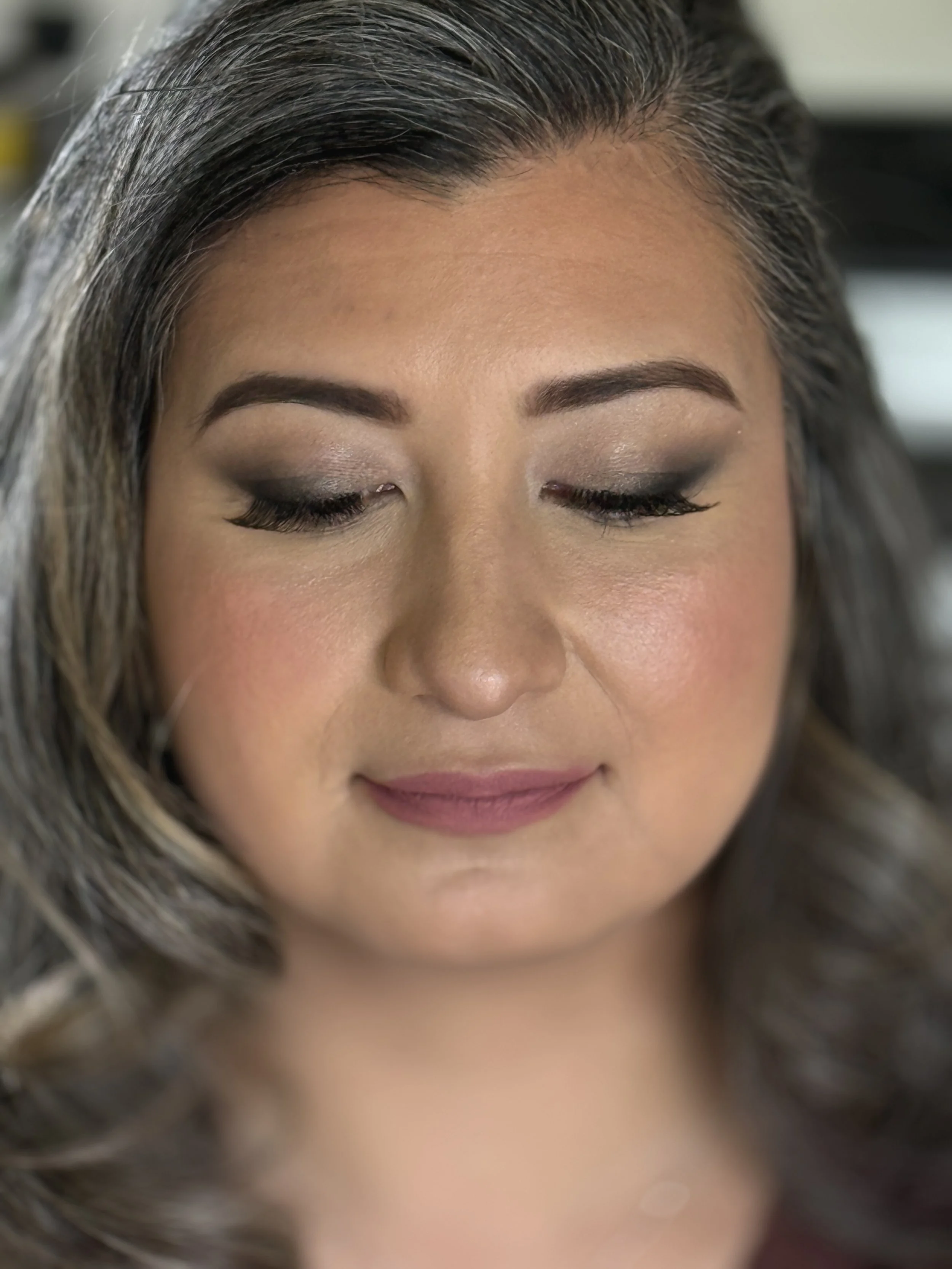 Close-up of a woman's face with closed eyes, showing her makeup and grayish-brown hair.