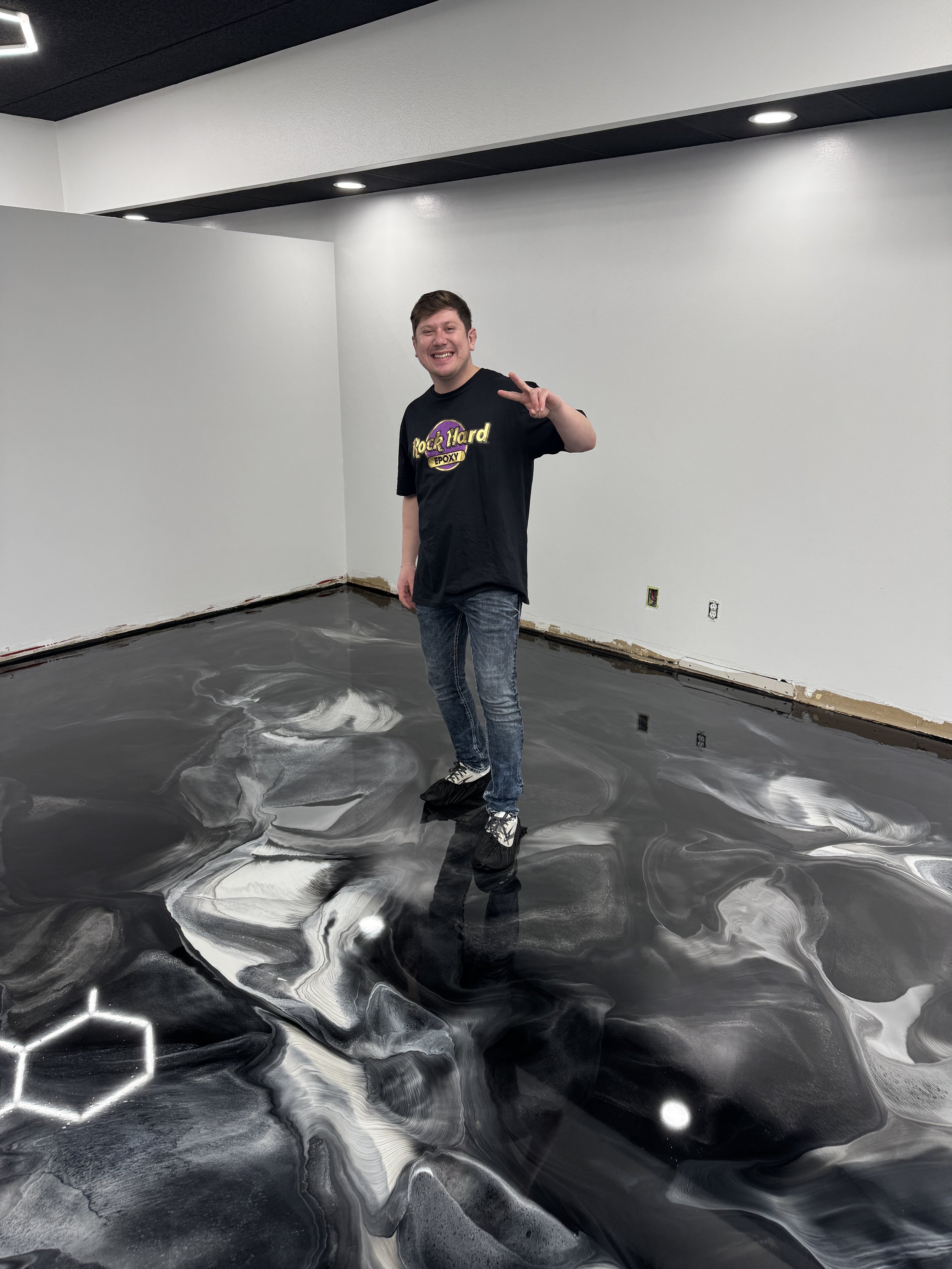 Person standing on a shiny black and white marbled floor in a modern white room, making a peace sign with their hand.