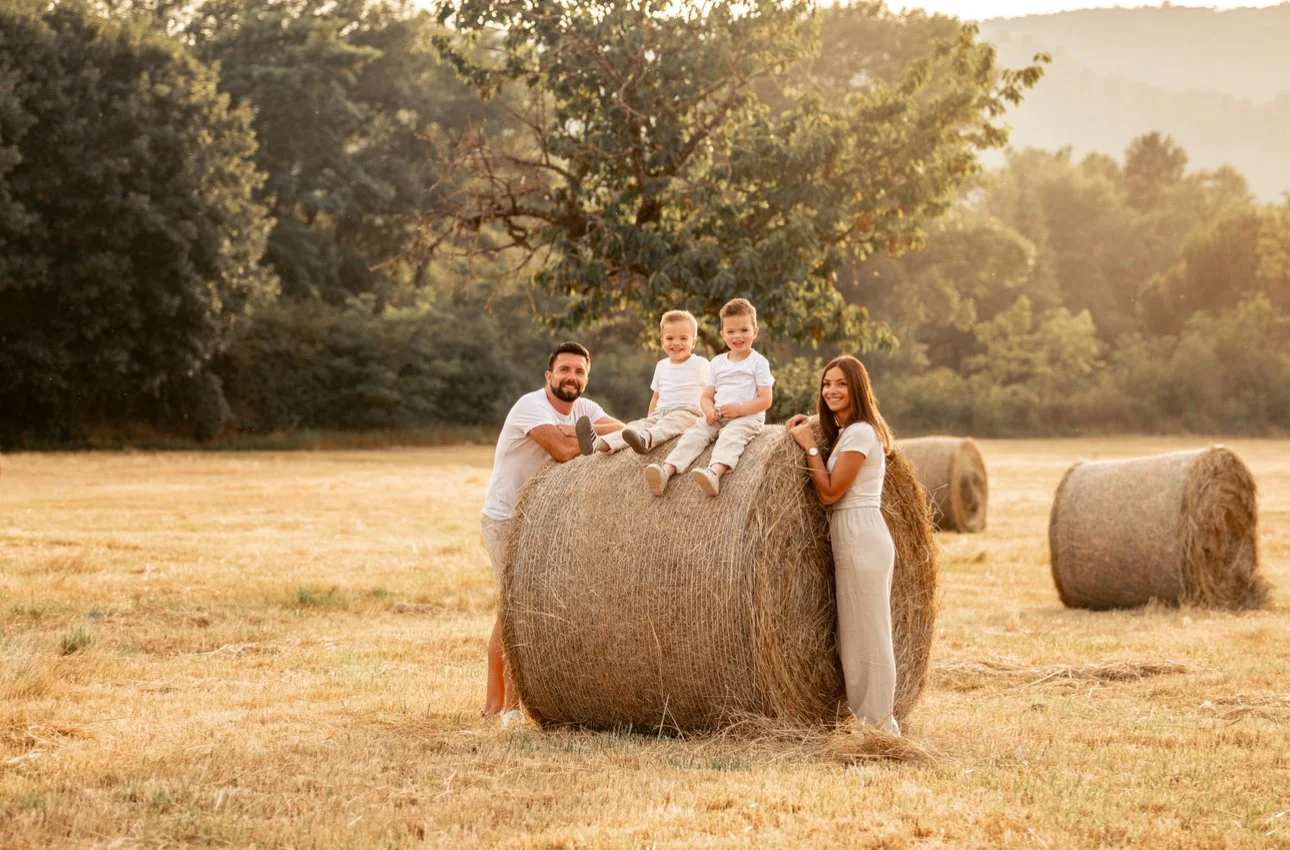 Une famille de quatre personnes dans un champ avec des bottes de foin, lors du coucher de soleil.