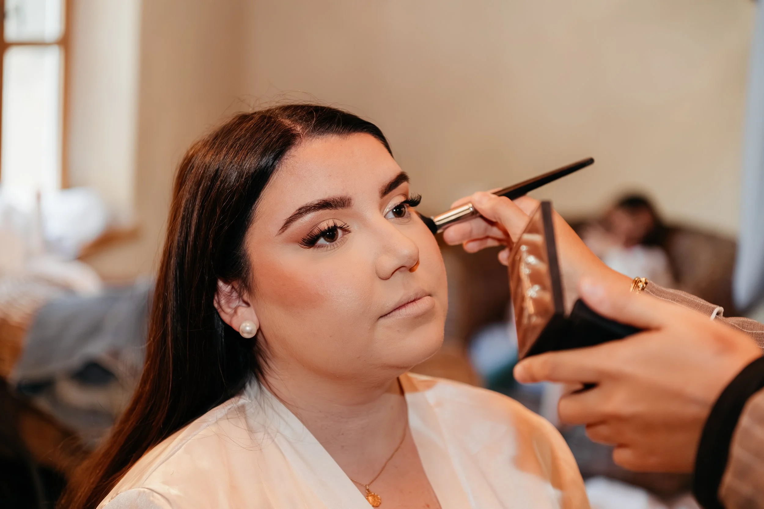 Une femme reçoit un maquillage de la part d'un artiste lors d'une séance de maquillage à l'intérieur.