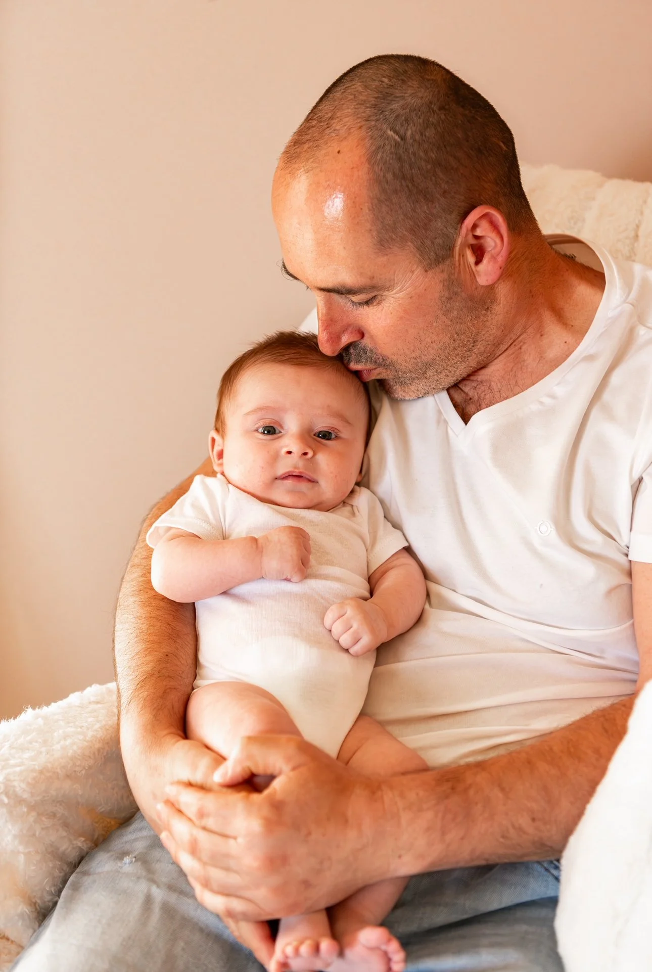 Un homme tient un bébé dans ses bras, il lui fait un câlin, dans un cadre intérieur chaleureux.