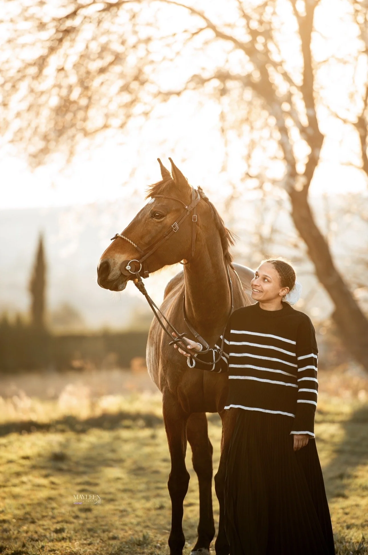 Une femme souriante se tenant à côté d'un cheval en plein air au coucher du soleil.
