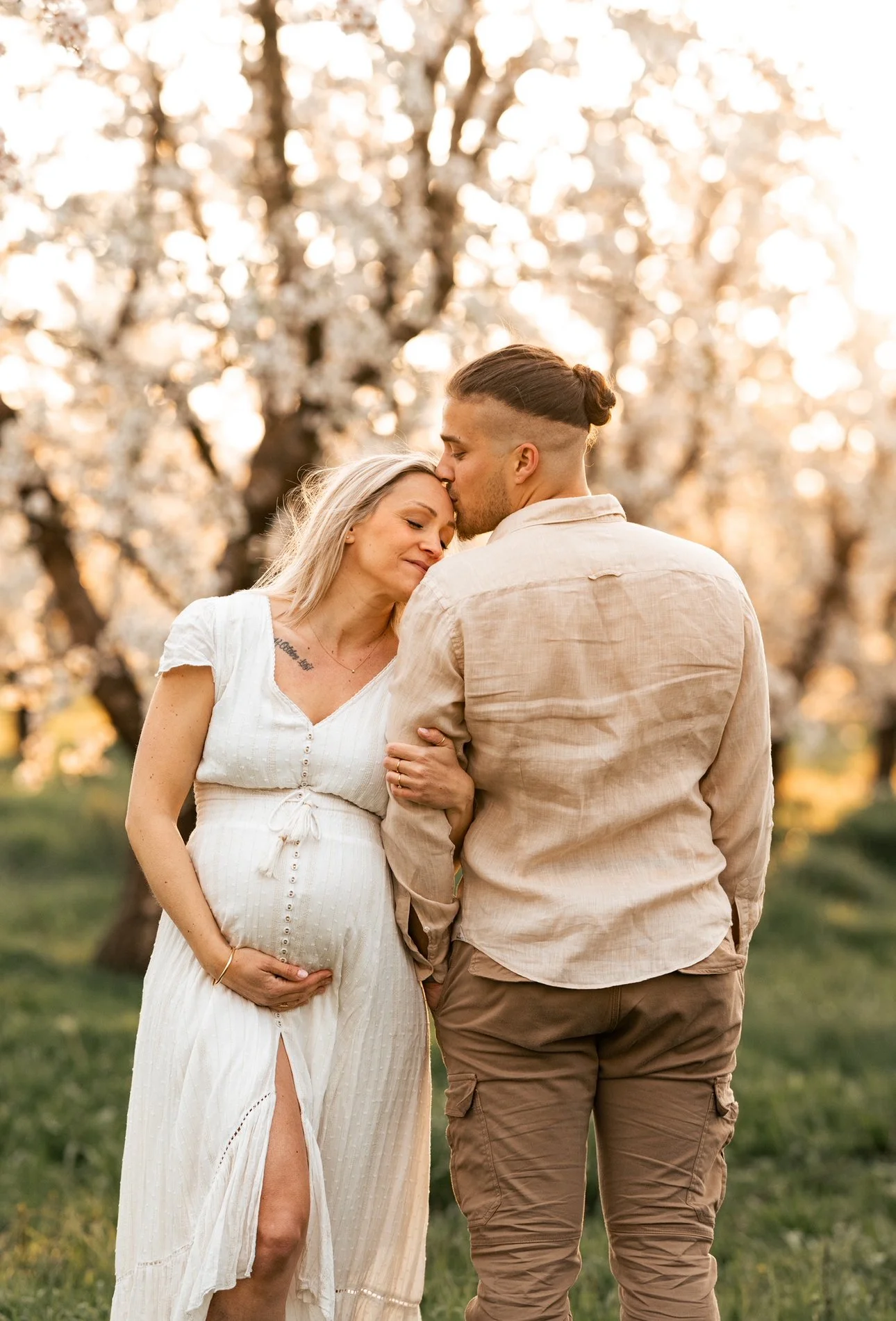Un couple, dont la femme enceinte, dans un parc avec des cerisiers en fleurs, lors du coucher du soleil.