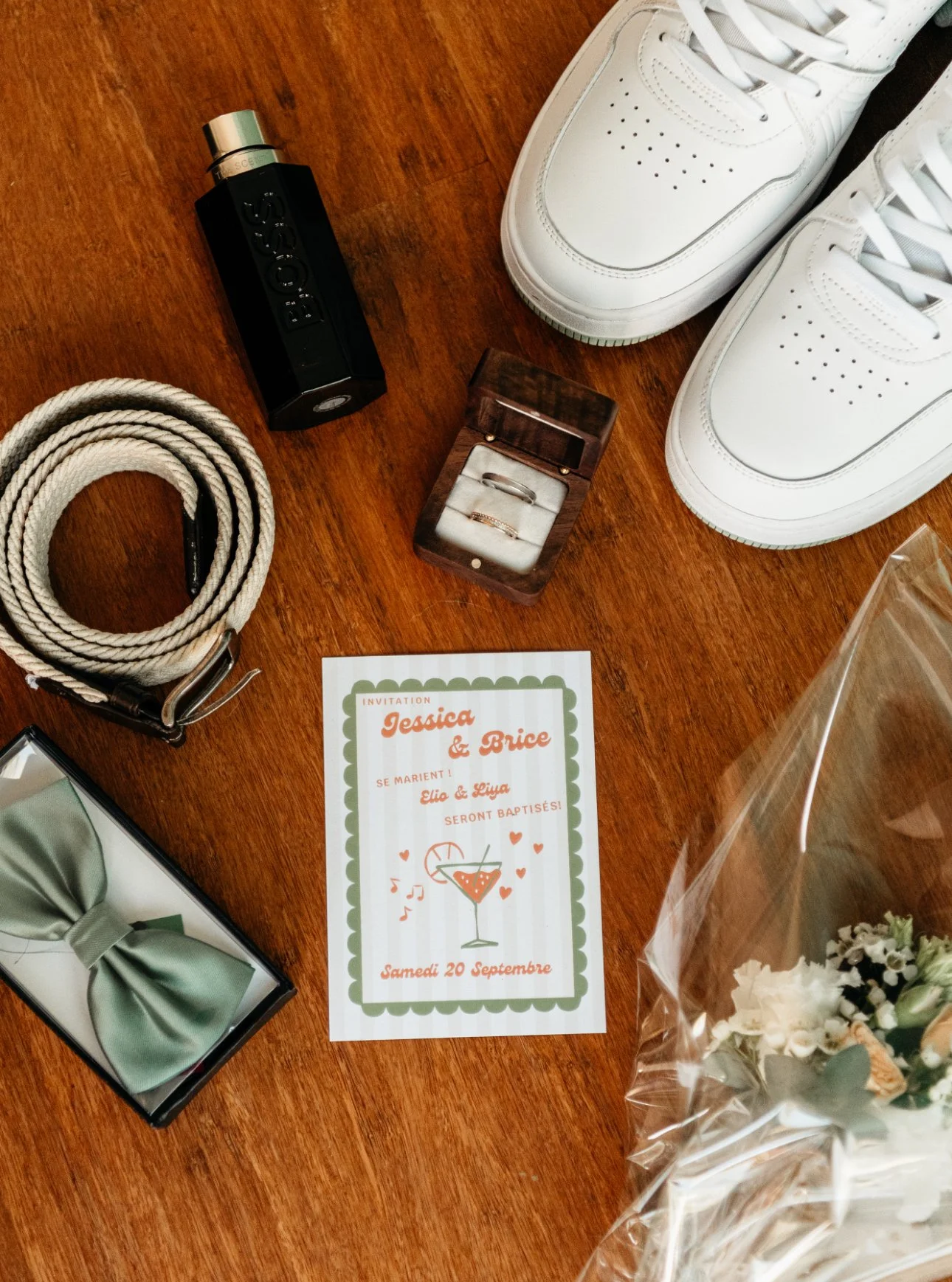 Invitation à un mariage, un flacon de parfum, une ceinture, une boîte à alliances, une paire de baskets blanches, un nœud papillon vert, une bouquet de fleurs, un spray de parfum, une carte d'invitation