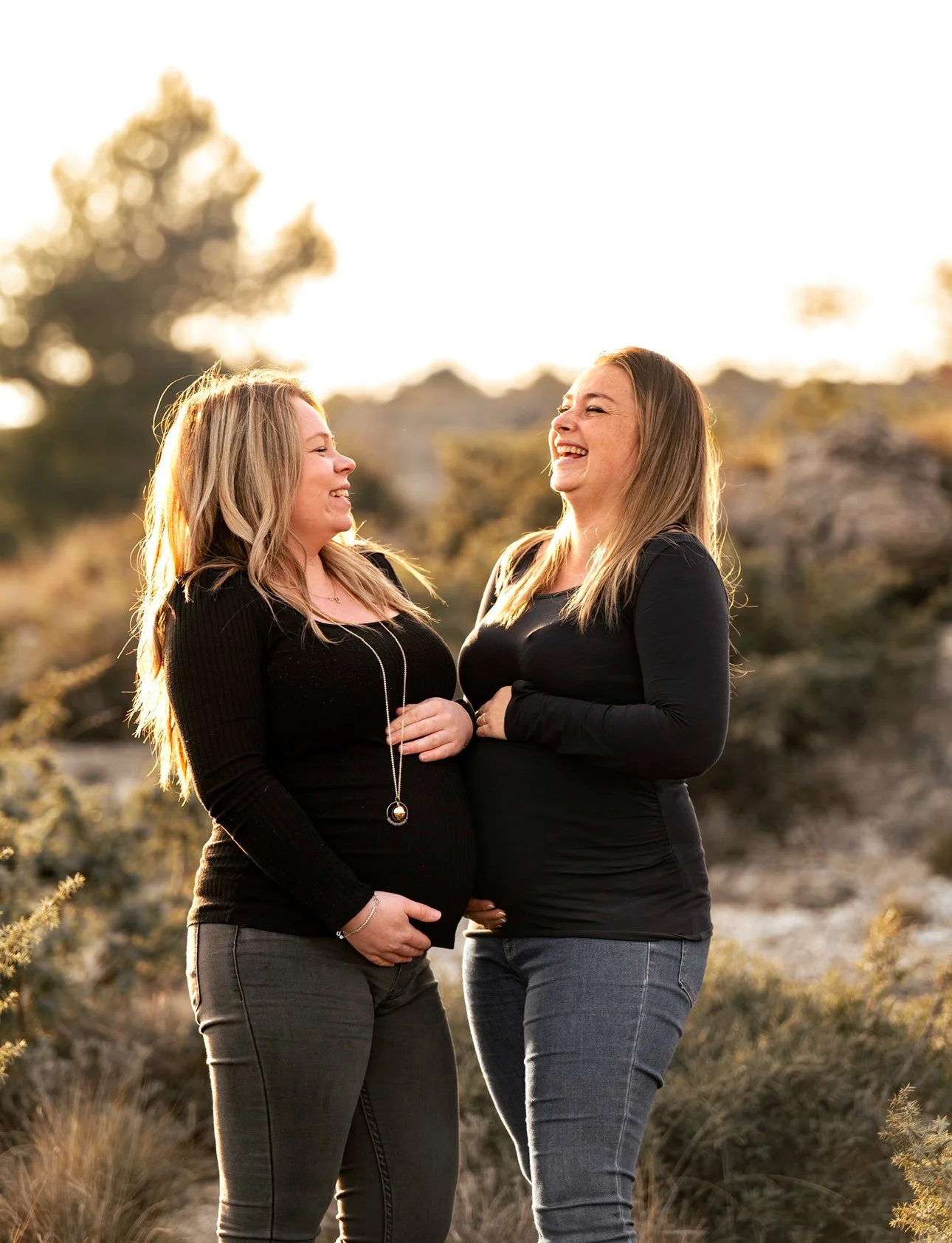 Deux femmes souriantes et se tenant la main devant un décor naturel au coucher du soleil.
