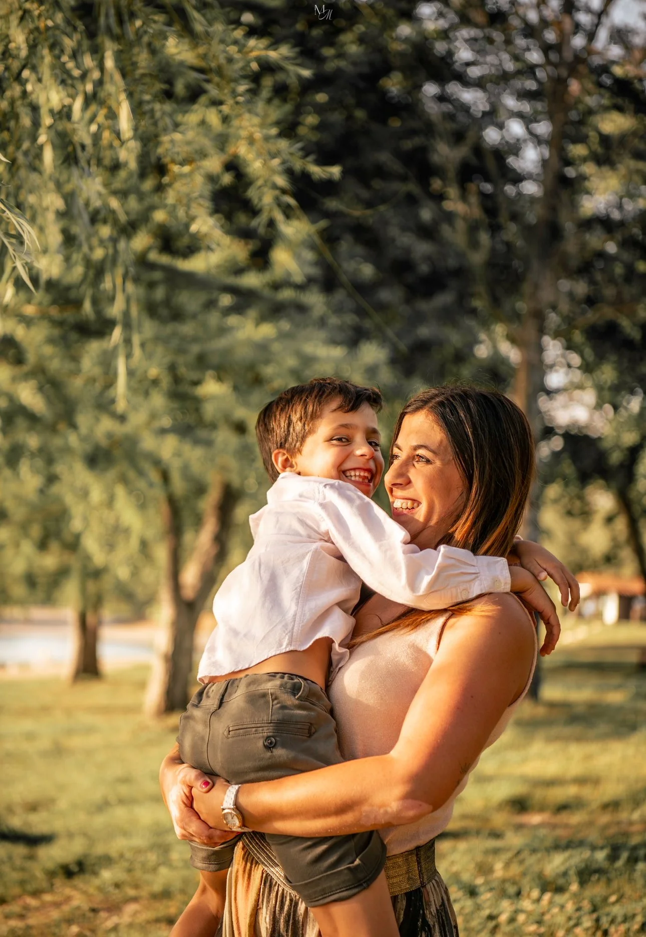 Une femme et un garçon souriant, l'enfant étant porté dans ses bras, dans un parc avec des arbres en arrière-plan.