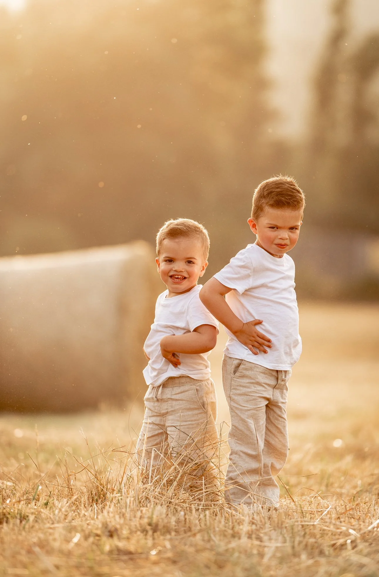 Deux jeunes garçons posant dans un champ en plein air, souriant et avec leurs mains sur leurs tailles, éclairés par une lumière chaude de fin de journée.