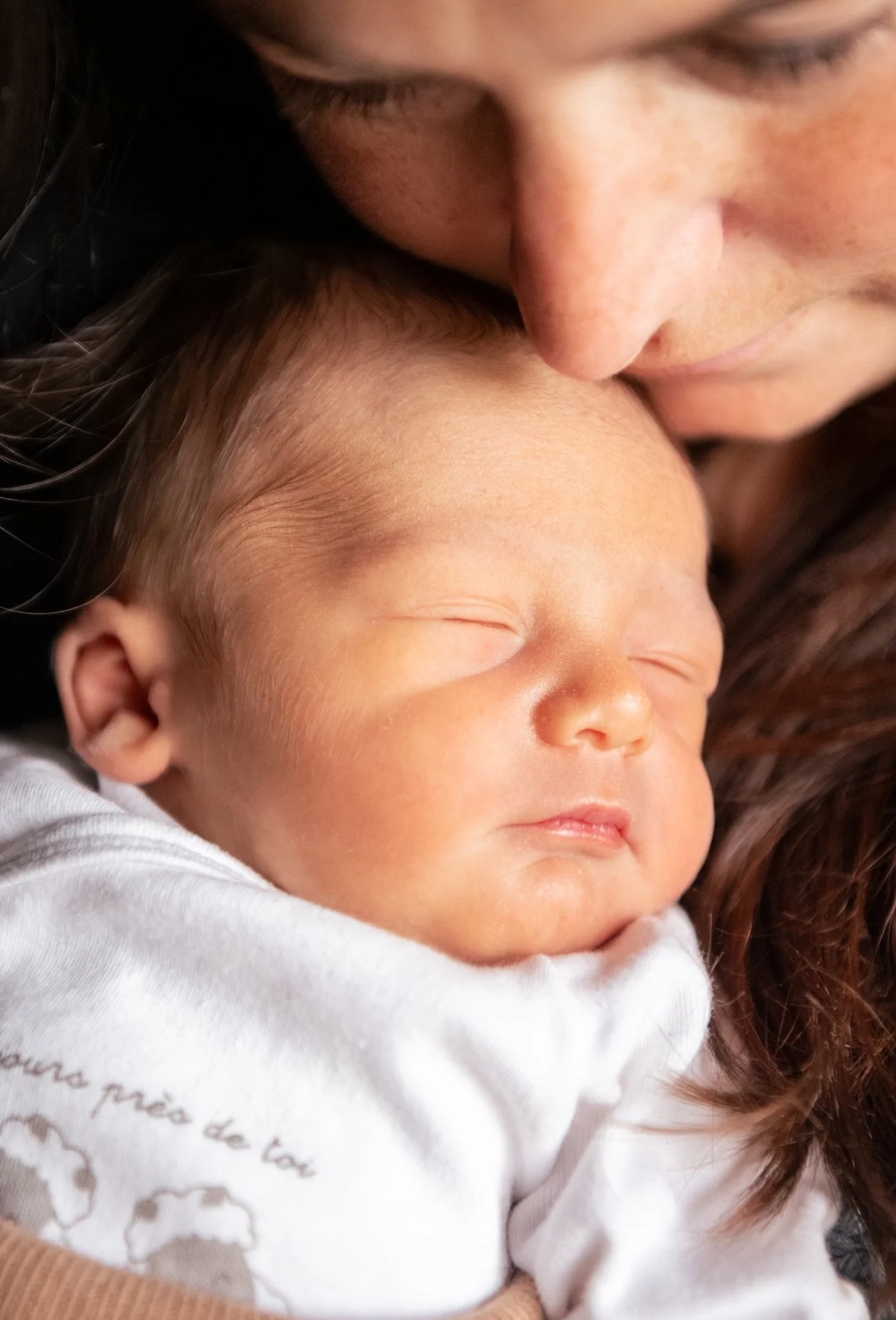 Un adulte ou une maman embrasse tendrement un bébé endormi à la naissance , tous deux avec la peau claire.