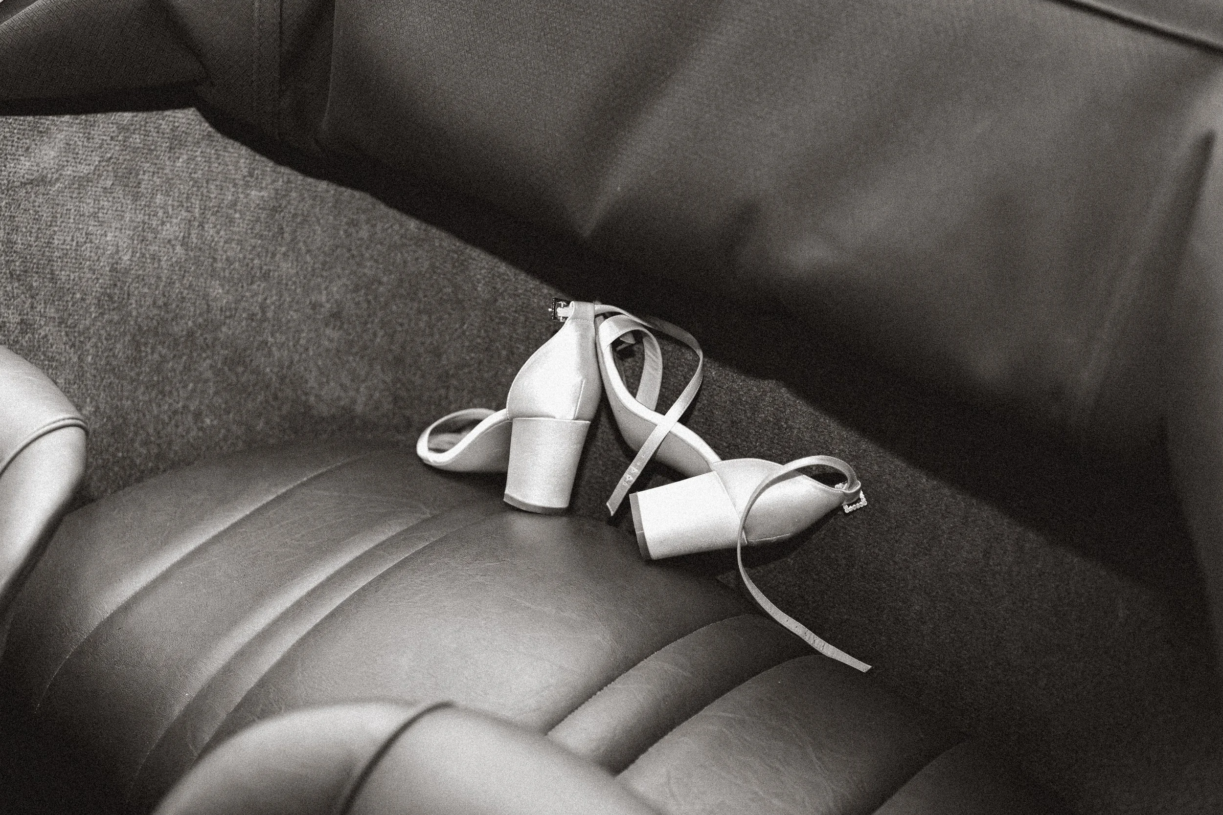 Une paire de chaussures à talons blancs repose sur le siège d'une voiture, dans un cadre en noir et blanc.