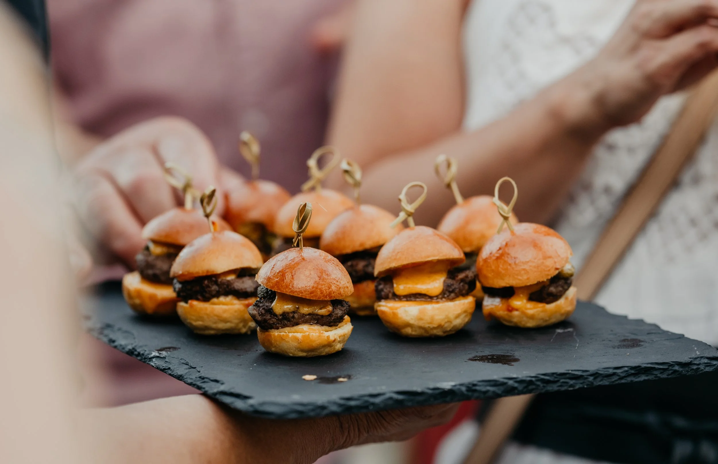 Mini burgers avec viande, fromage et sauce, garnis avec un cure-dent, présentés sur une plaque en ardoise vin d'honneur