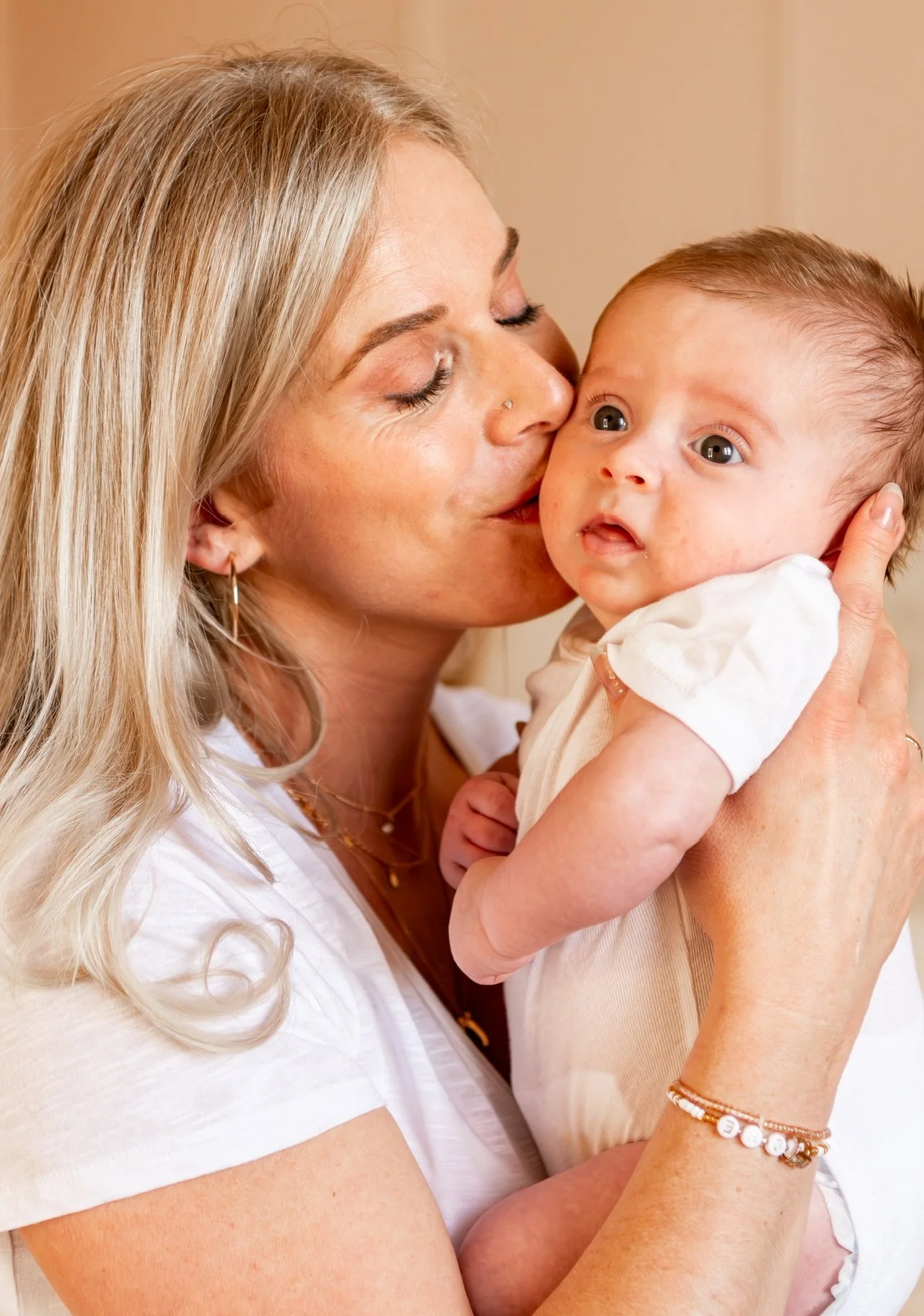 Une femme blonde embrasse tendrement un bébé dans ses bras.