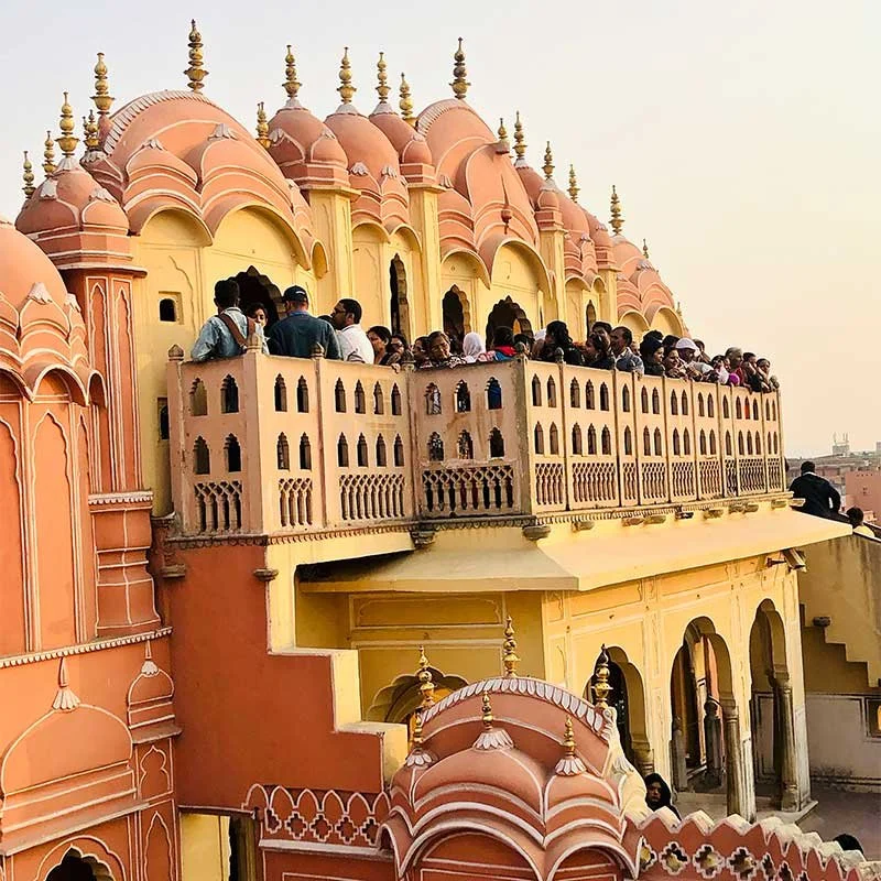 People standing on a terrace of a historic Indian palace with pink and yellow domed architecture