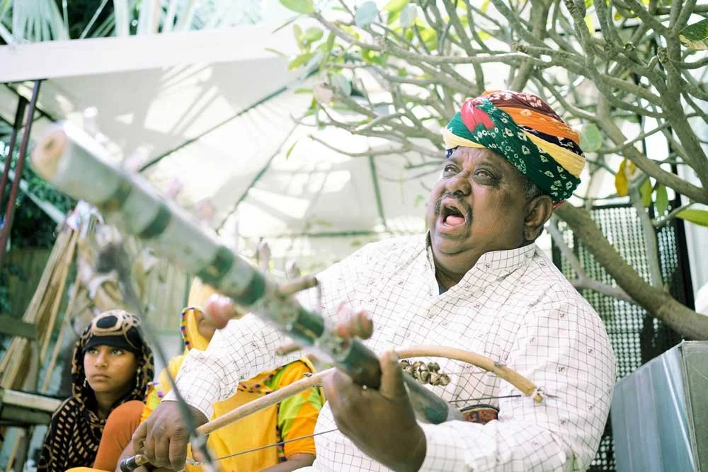 Man wearing a colorful turban playing a traditional musical instrument outdoors