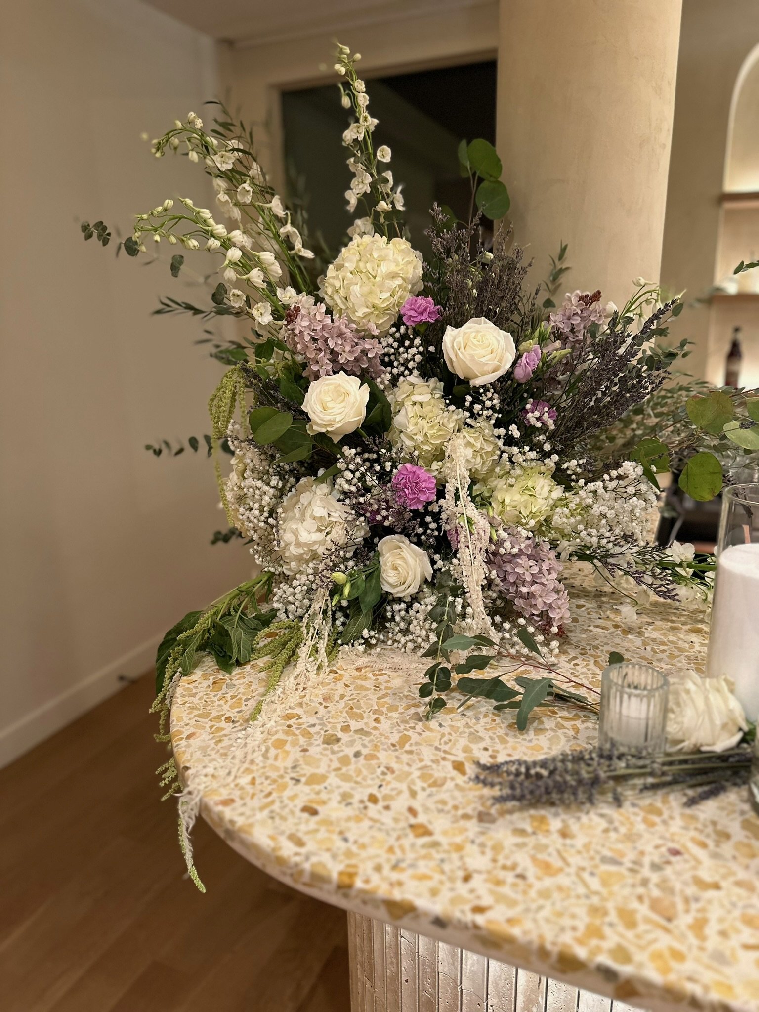 Floral arrangement with white roses and purple accents on a marble table indoors.