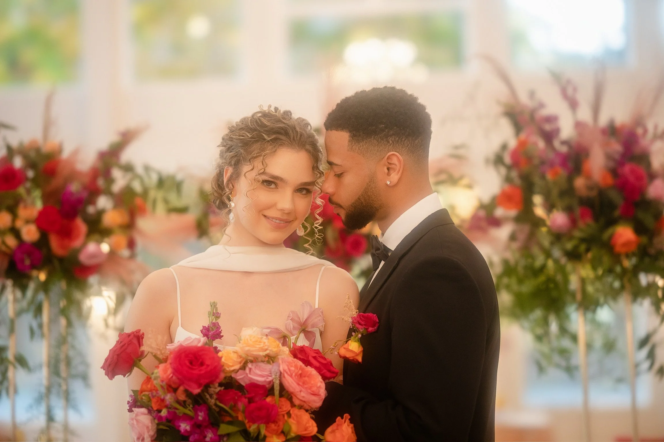 Bride and groom with colorful flower bouquet, smiling and embracing at wedding ceremony.