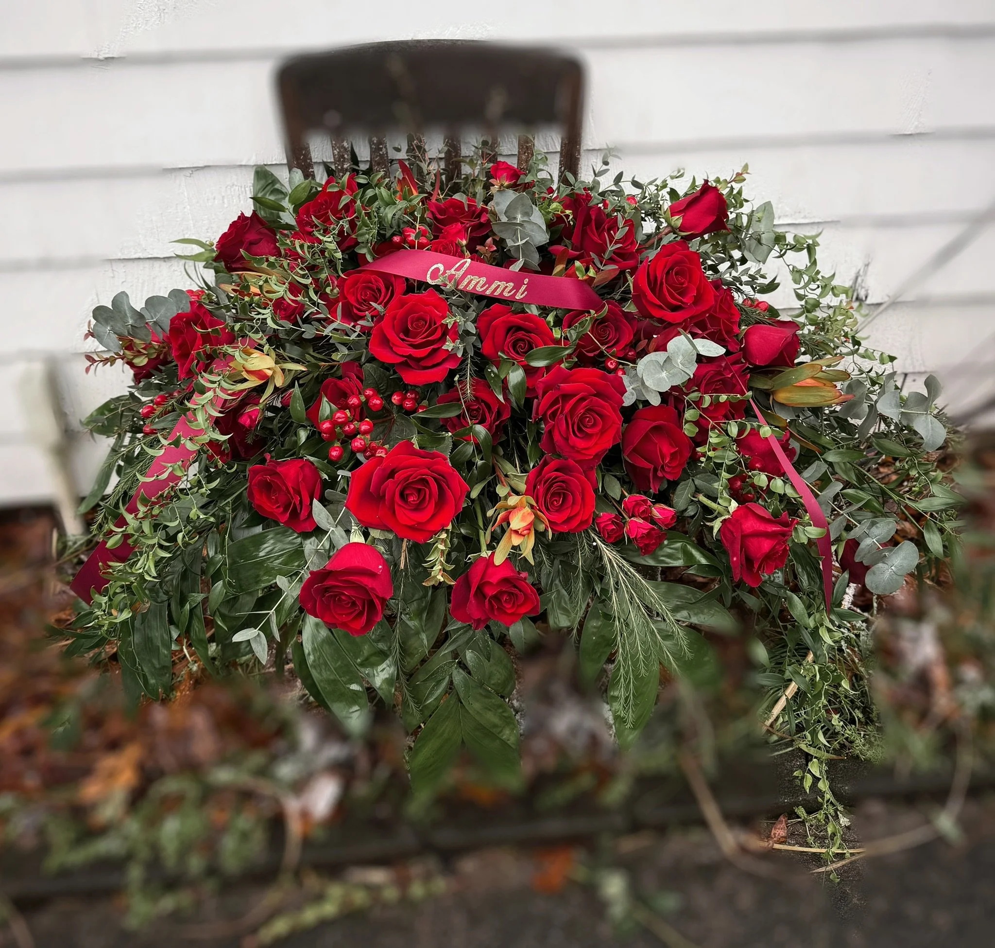 A floral arrangement of red roses with greenery on a wooden chair.