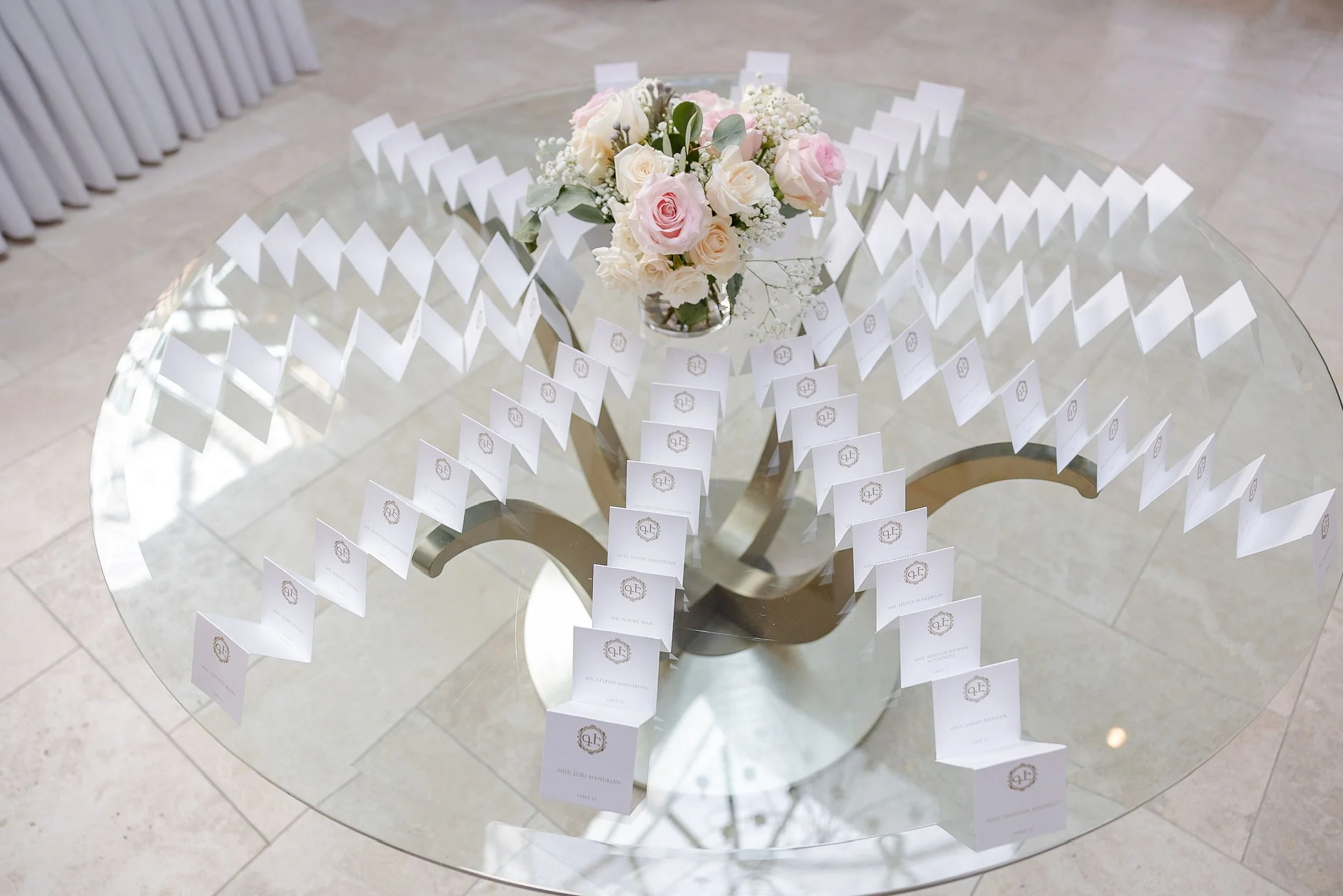 Table with a floral centerpiece and a display of wedding place cards arranged in rows.