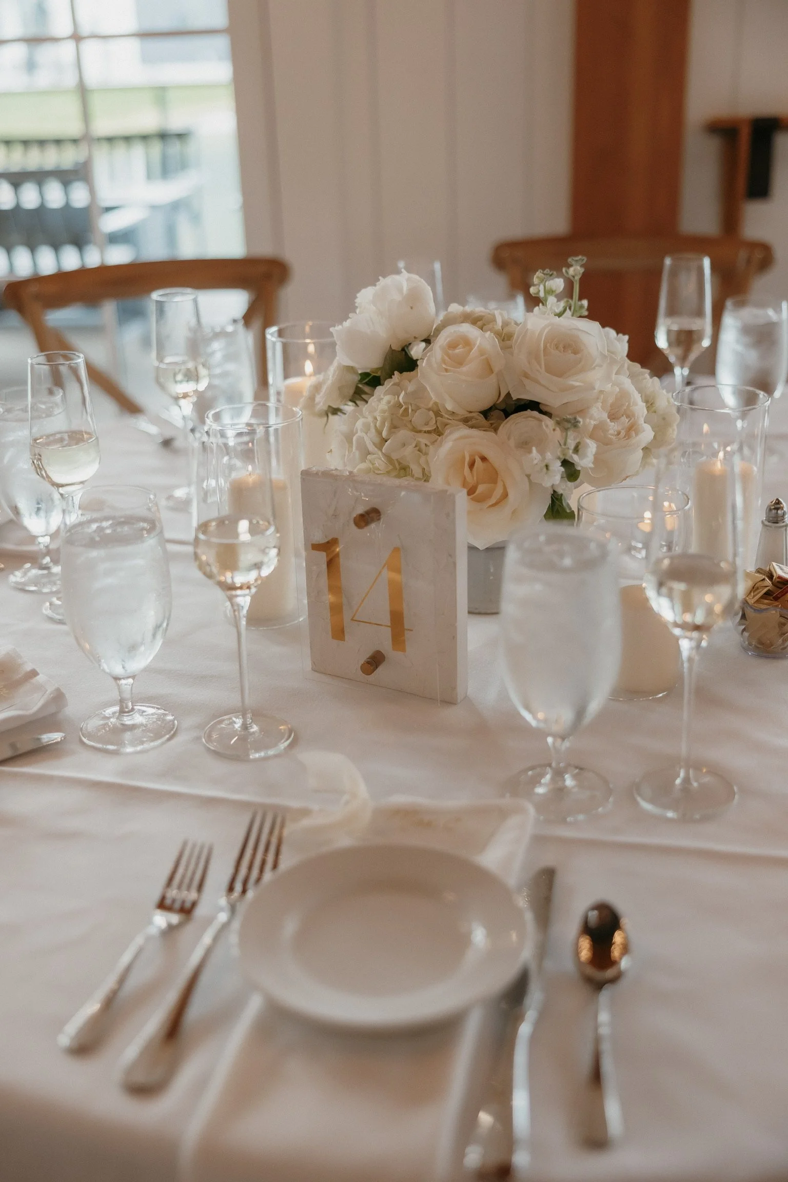 Elegant table setting with white floral centerpiece, table number 14, wine glasses, and candles.
