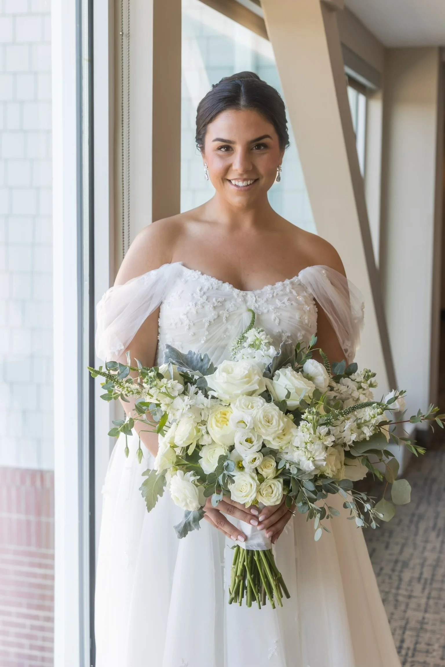 Bride in off-shoulder wedding dress holding a bouquet of white flowers.