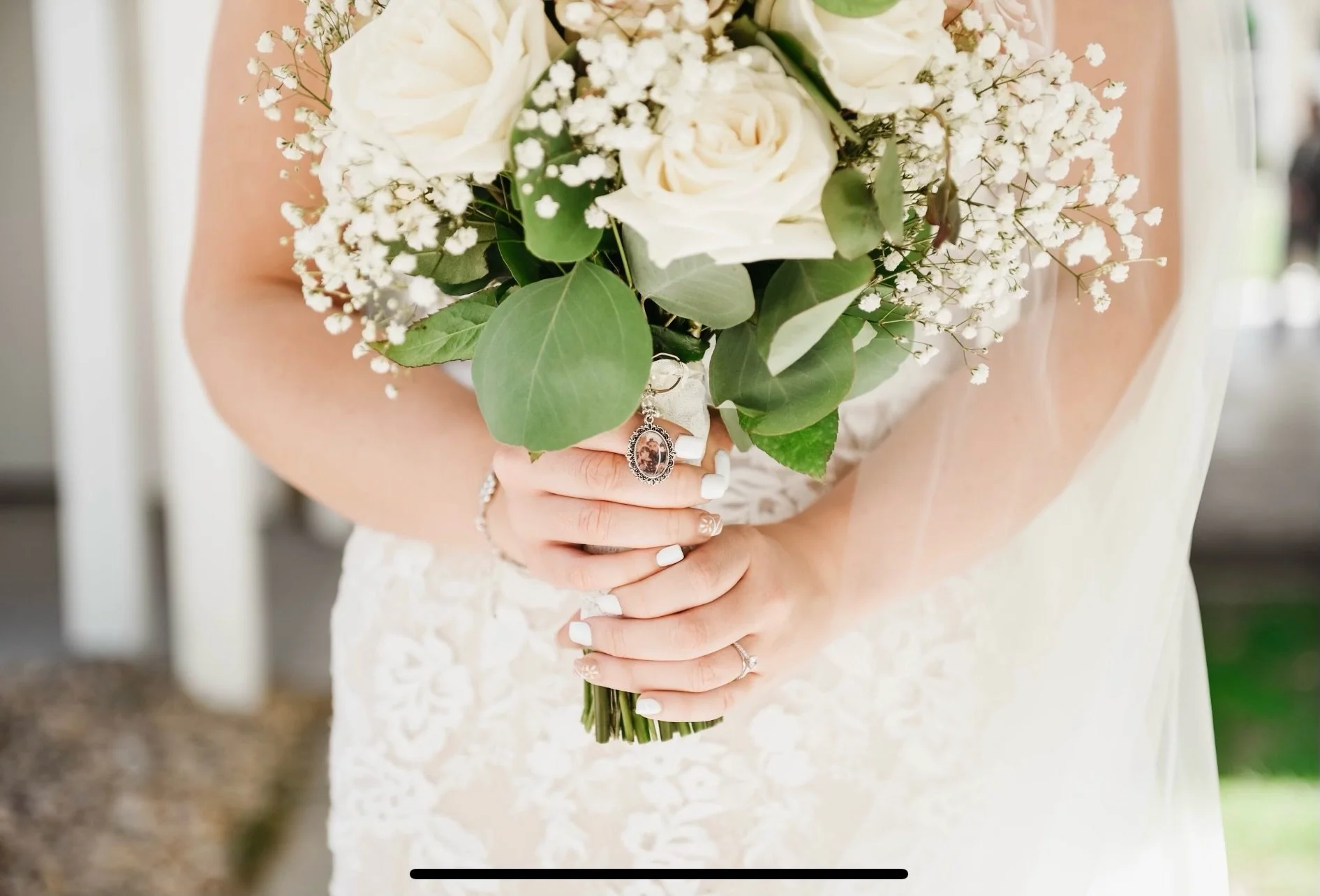 Bride holding a bouquet of white roses and baby's breath with a cameo pendant attached to stems.