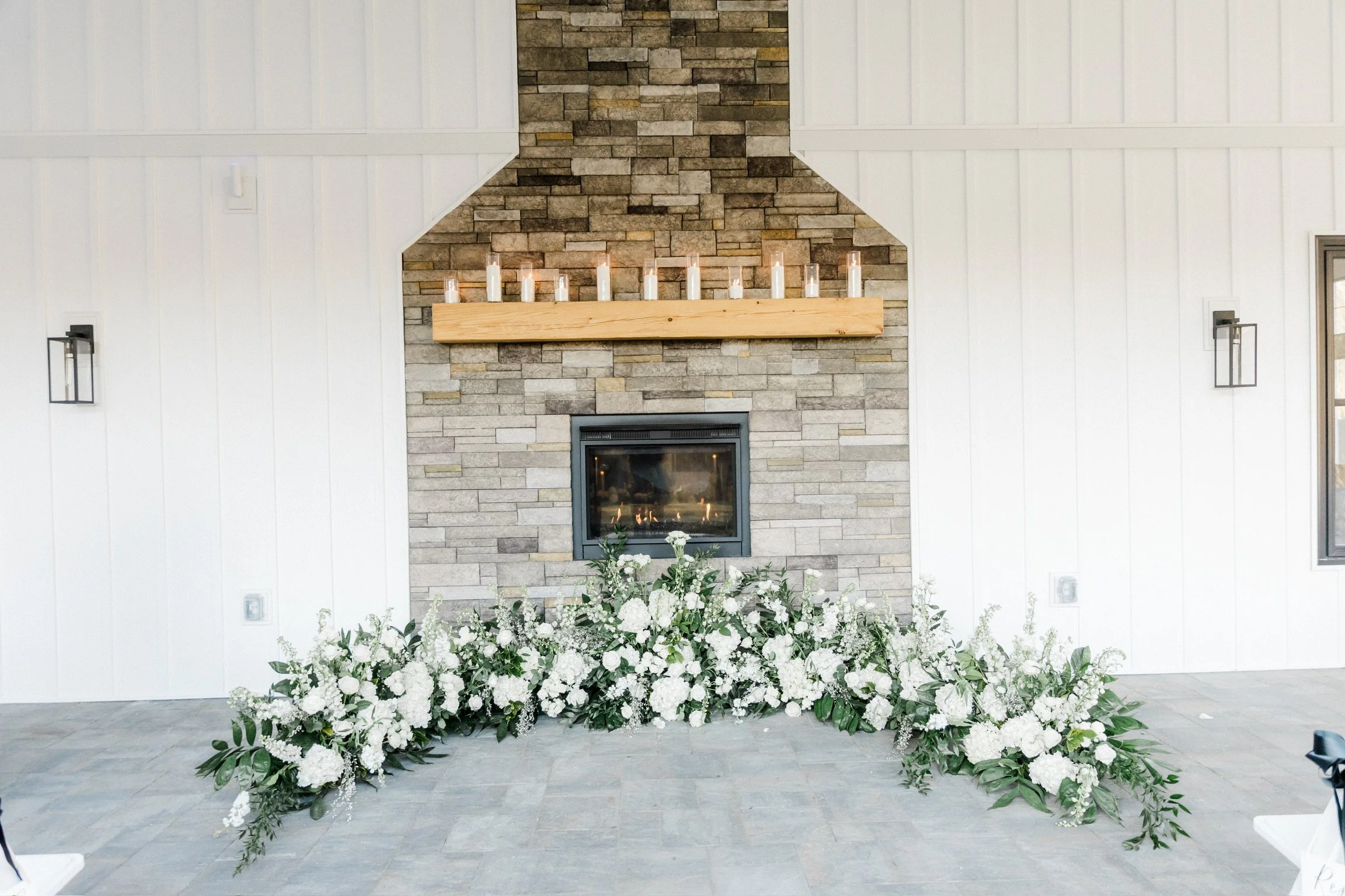 Stone fireplace with candles on wooden mantel and white flower arrangement below
