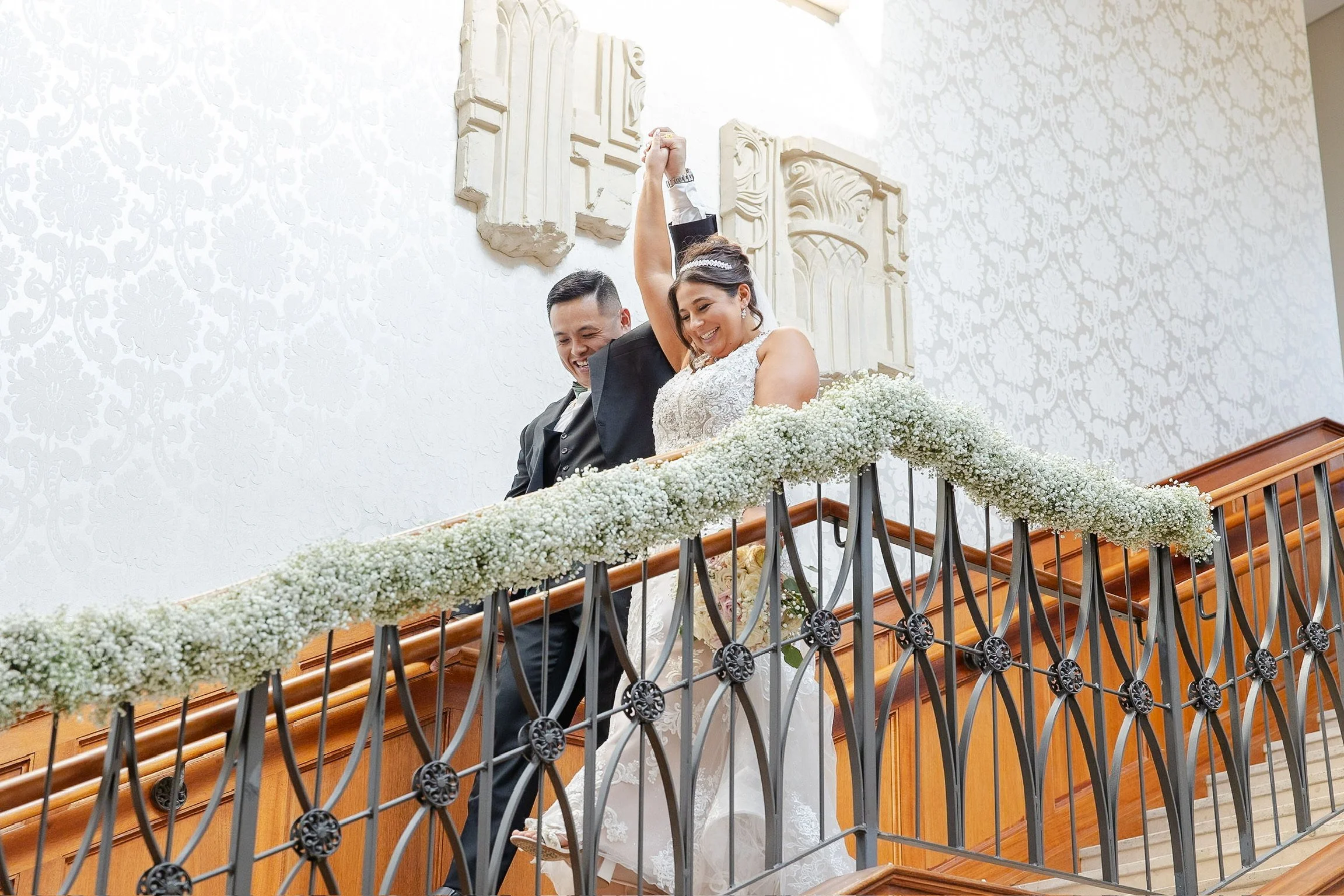 Bride and groom celebrating on a staircase with floral decorations.
