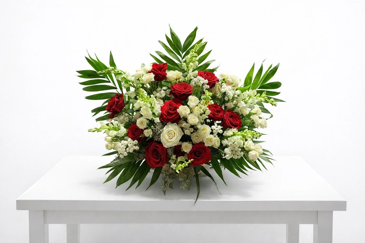 Red and white floral arrangement with green leaves on a white table against a white background.