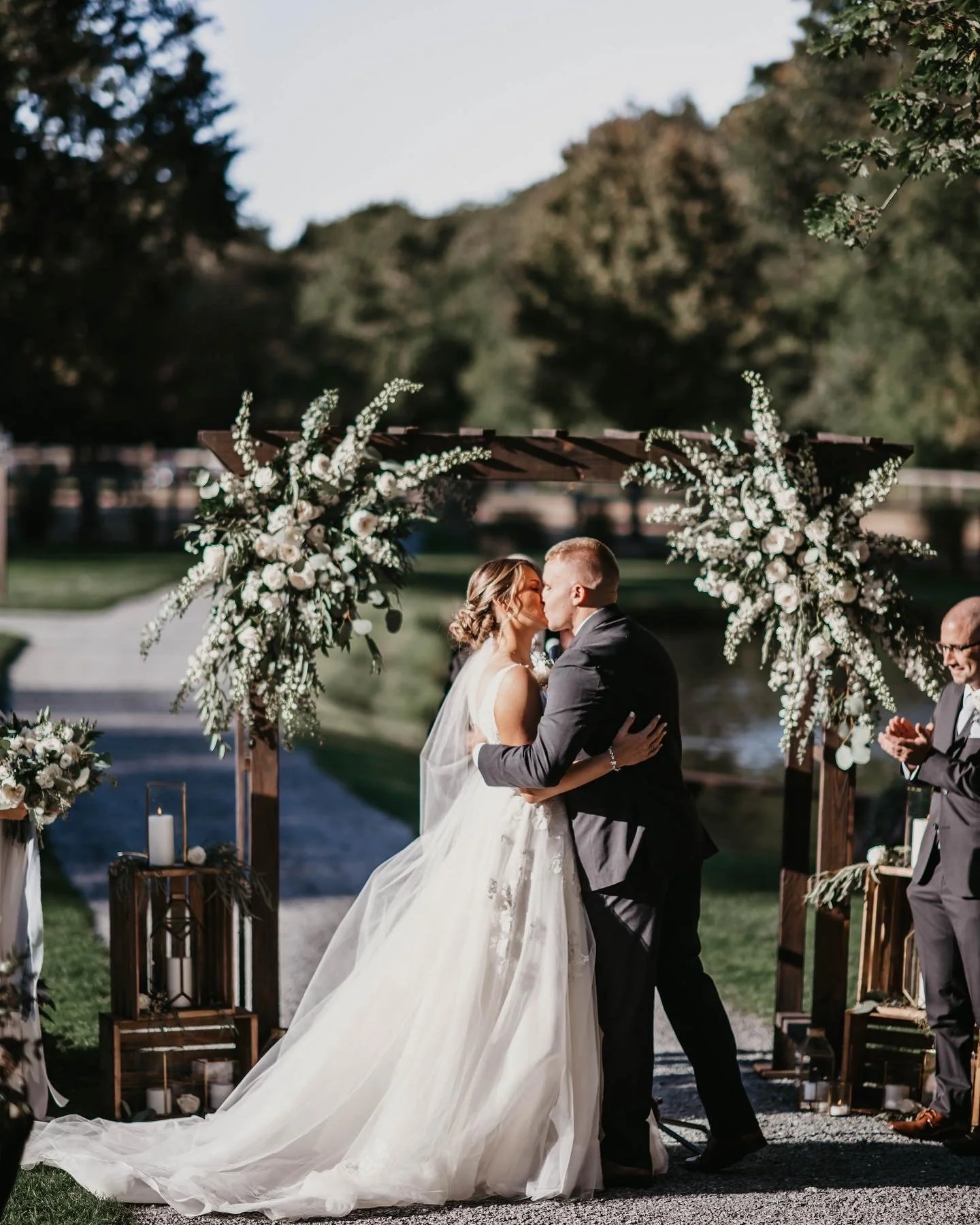Couple kissing at outdoor wedding ceremony under floral arch.