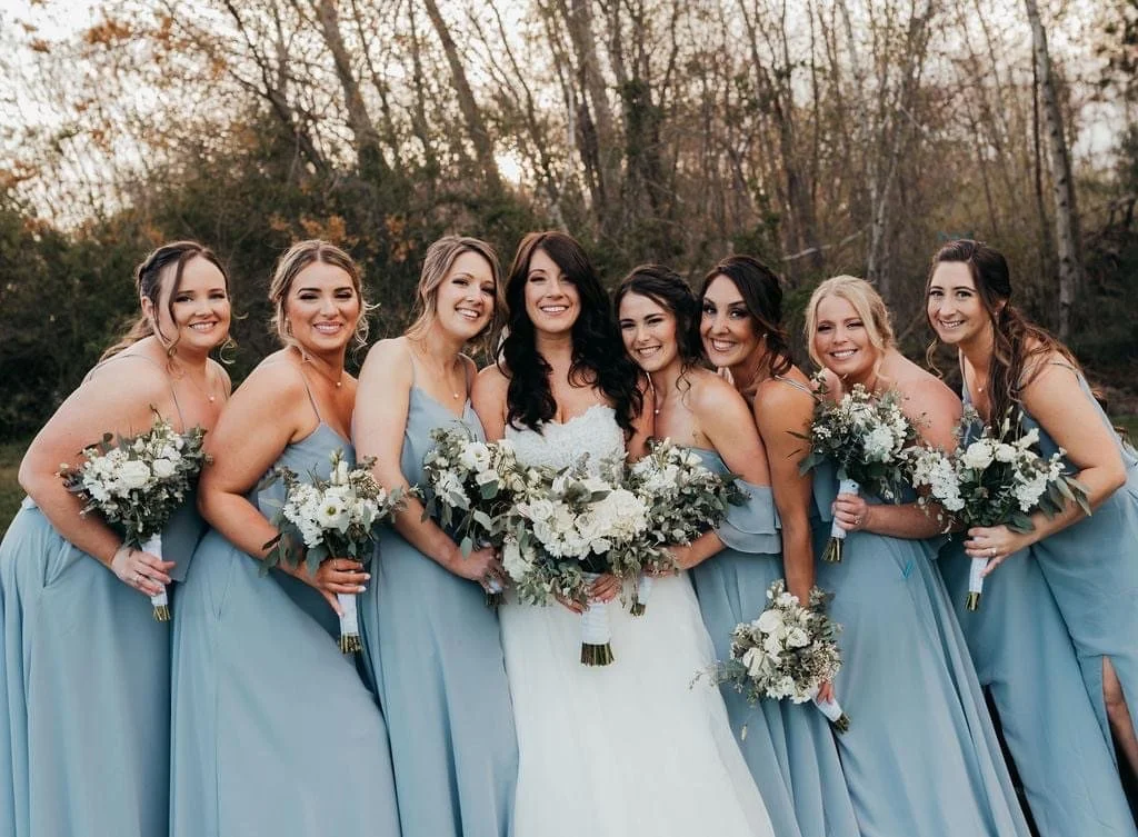 Bride with bridesmaids wearing matching blue dresses and holding bouquets, outdoors