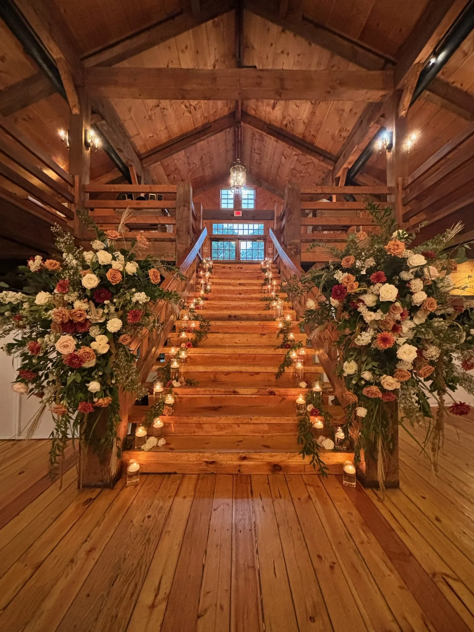 Rustic wooden staircase with candles and floral arrangements, inside a wooden barn venue.