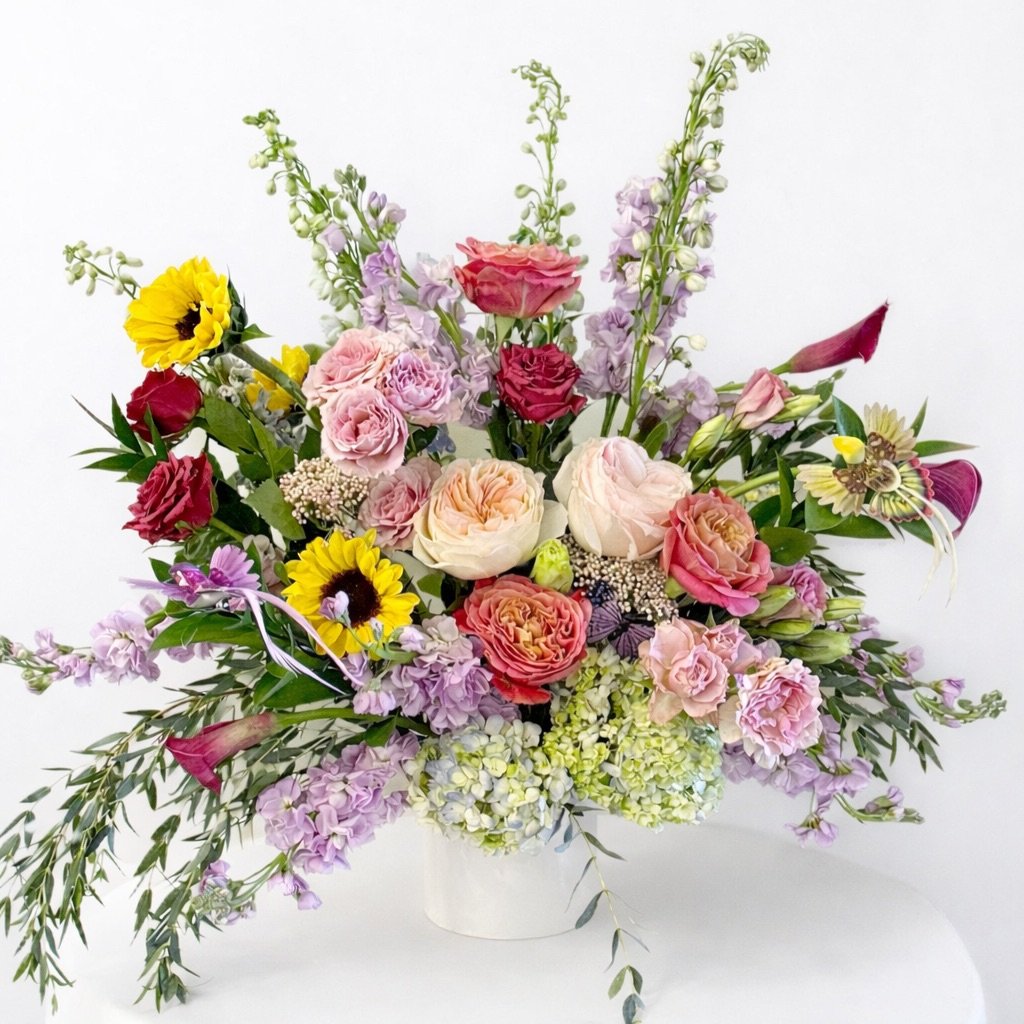 Colorful flower arrangement with roses, sunflowers, and hydrangeas in a white vase.