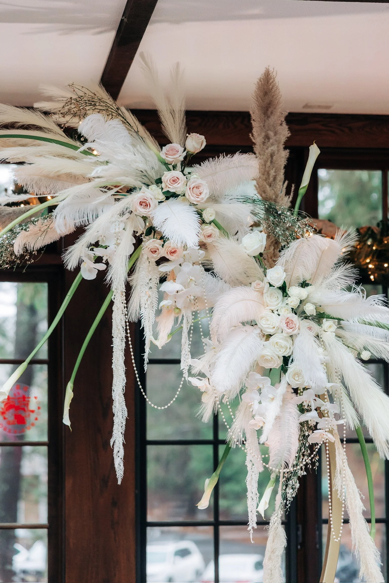 Floral arrangement with white feathers, pampas grass, blush roses, and pearls.