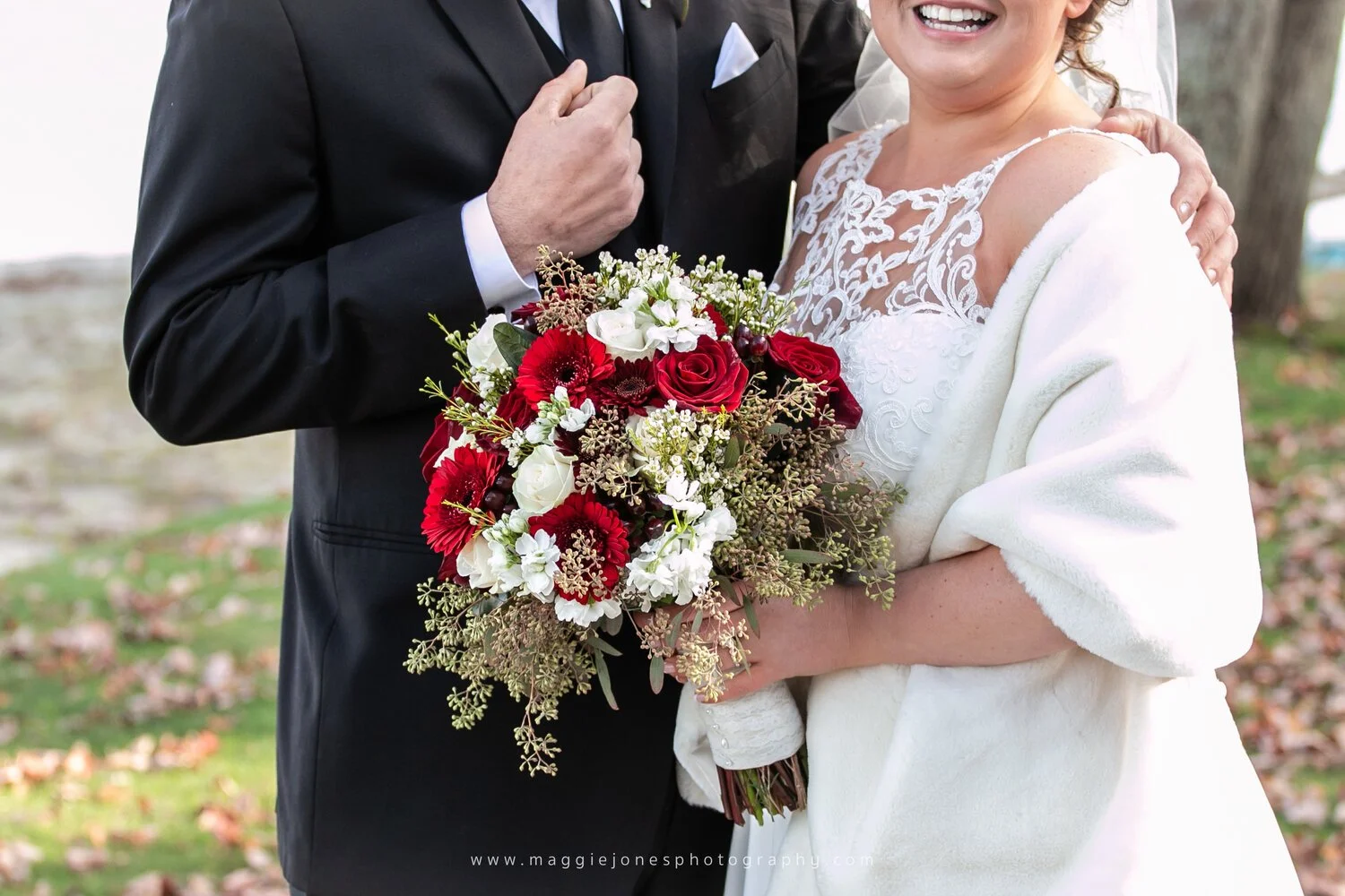 Bride and groom holding a bouquet of red and white flowers, dressed in formal wedding attire.