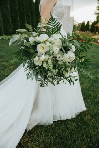 Bride holding a white floral bouquet outdoors on grass