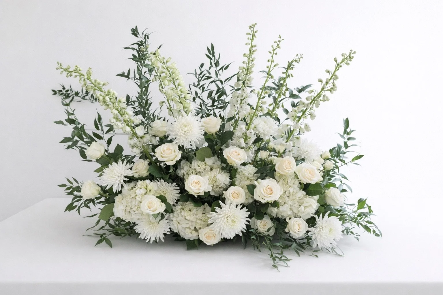 White floral arrangement with roses, dahlias, and greenery on white background.