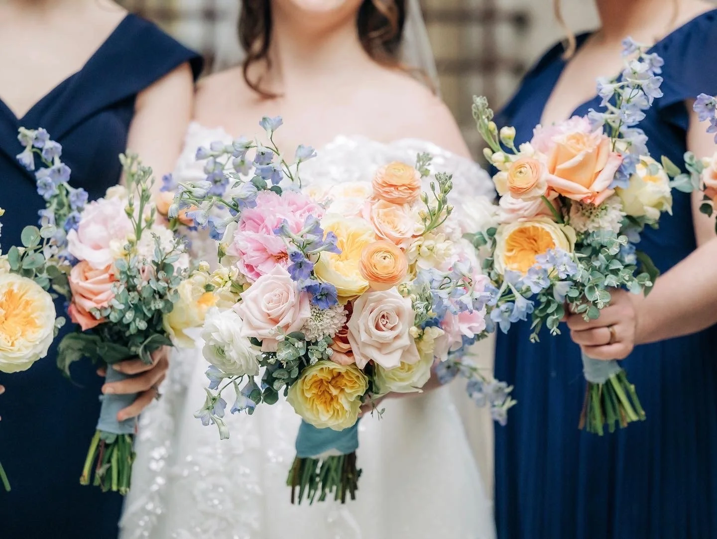 Bridesmaids and bride holding colorful flower bouquets with roses and delphiniums.